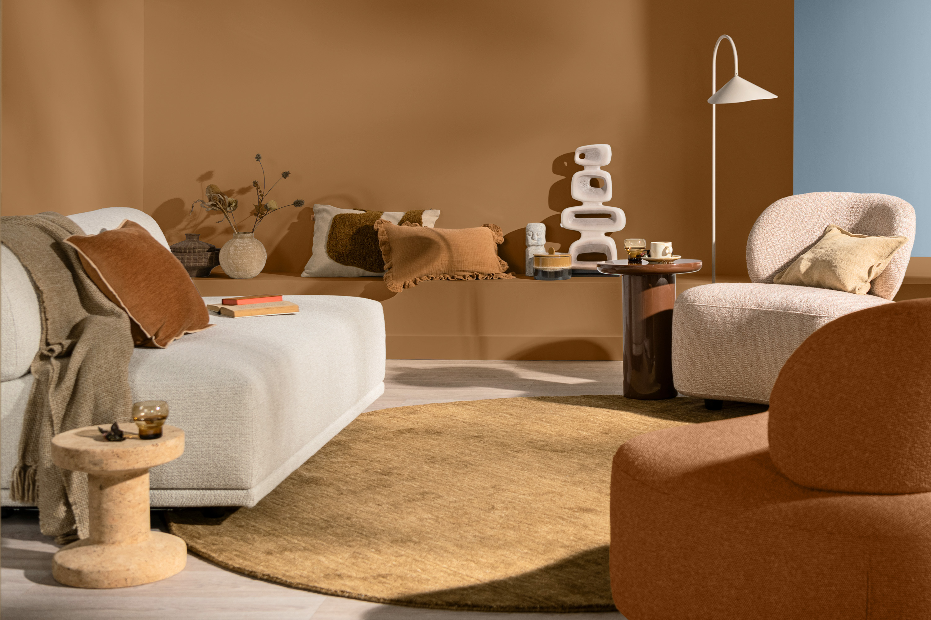 stue med hvit sofa, rundt brunt teppe og brun vegg. blått rom ved siden av