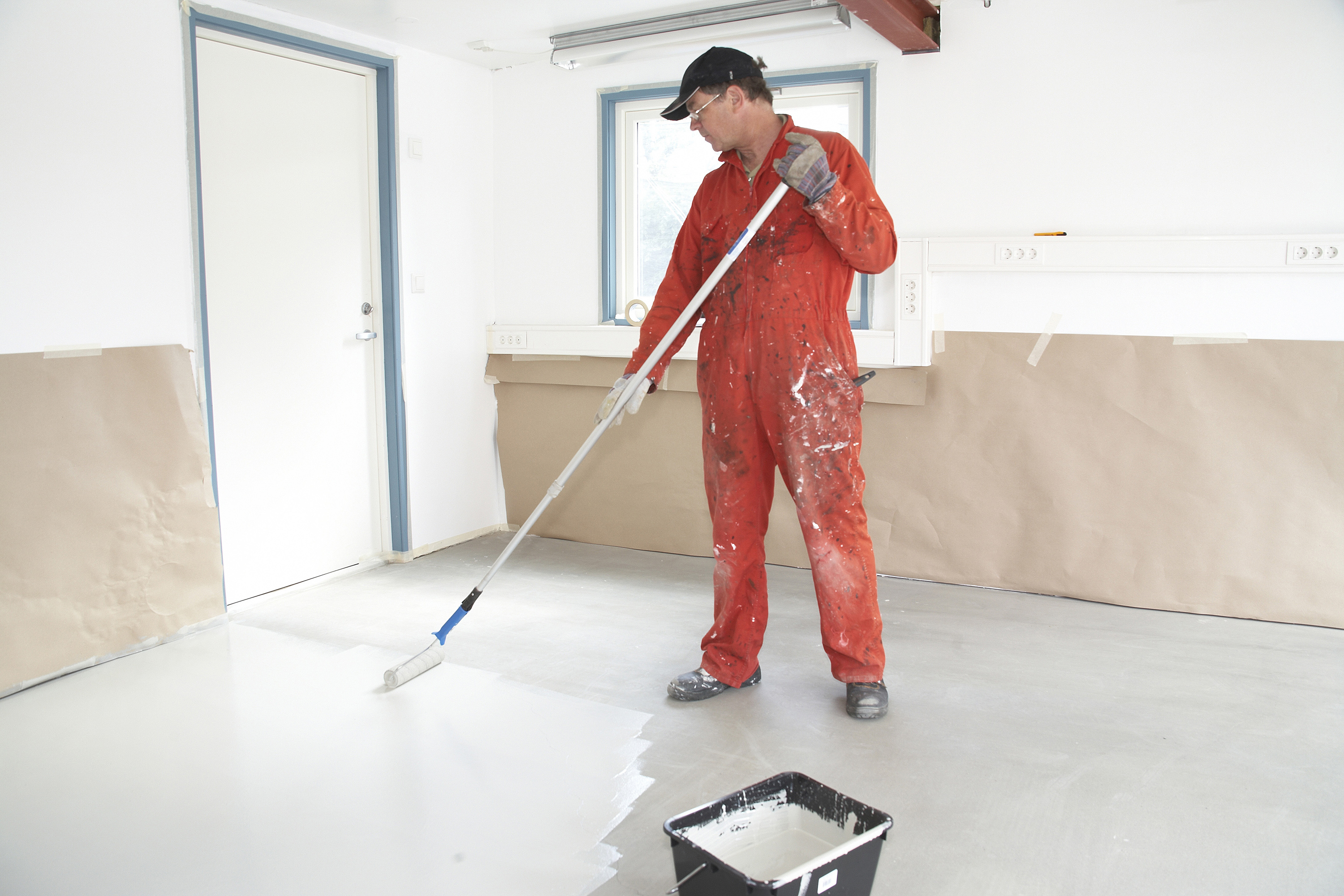 Mann i kjeledress ruller epoksymaling i en garasje