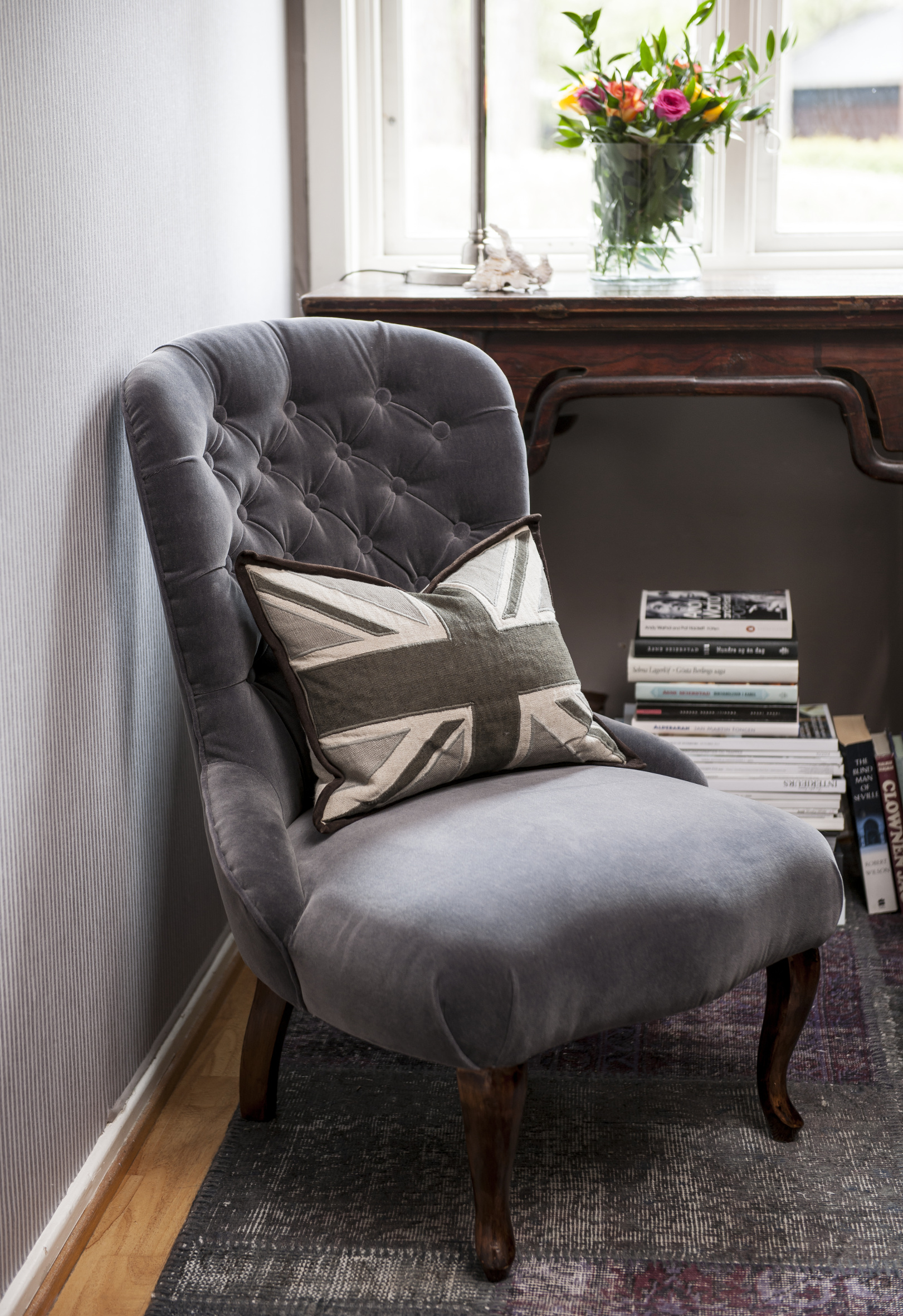 En gammel, hyggelig stol i ny drakt; matt, grå velur, vel tilpasset de øvrige fargene. 