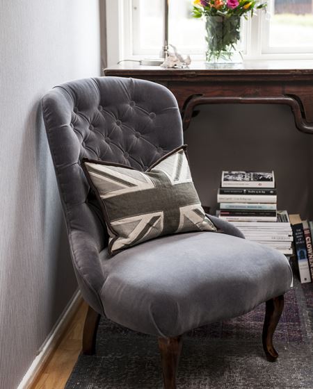 En gammel, hyggelig stol i ny drakt; matt, grå velur, vel tilpasset de øvrige fargene. 