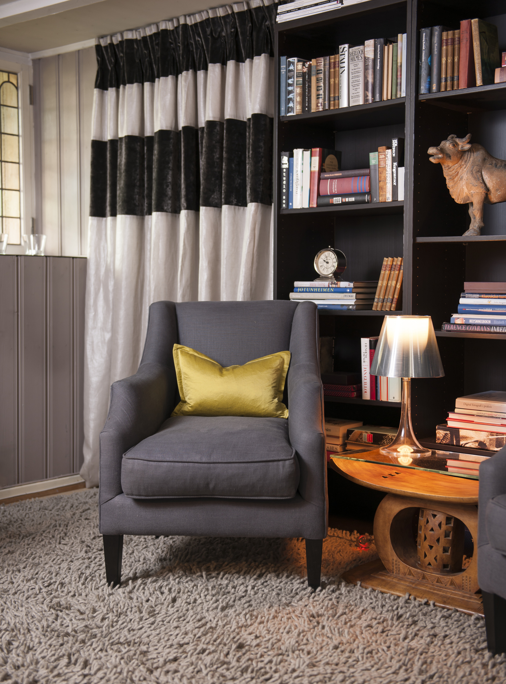 SKJULT GARDEROBE I motsatt ende av soverommet skjuler en fotsid gardin en nisje med et walk-in closet. Rolige, mørkladne farger i selskap med en gammel, gyllen, afrikansk krakk, som fungerer som bord og tilfører en varm farge.