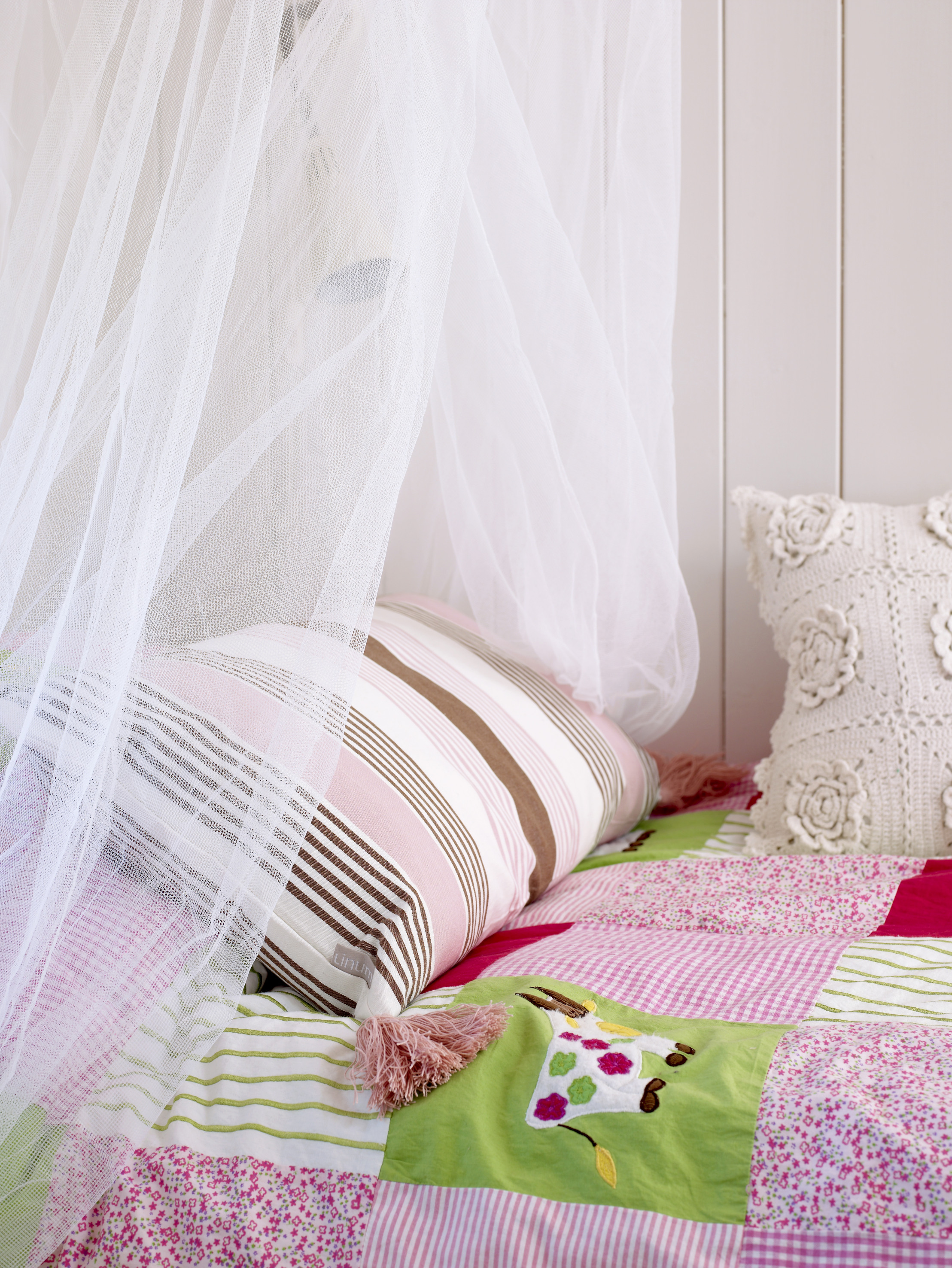 Anna har prinsesseslør over sengen sin og sengeteppe og puter i nyanser av rosa og grønt.