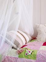 Anna har prinsesseslør over sengen sin og sengeteppe og puter i nyanser av rosa og grønt.