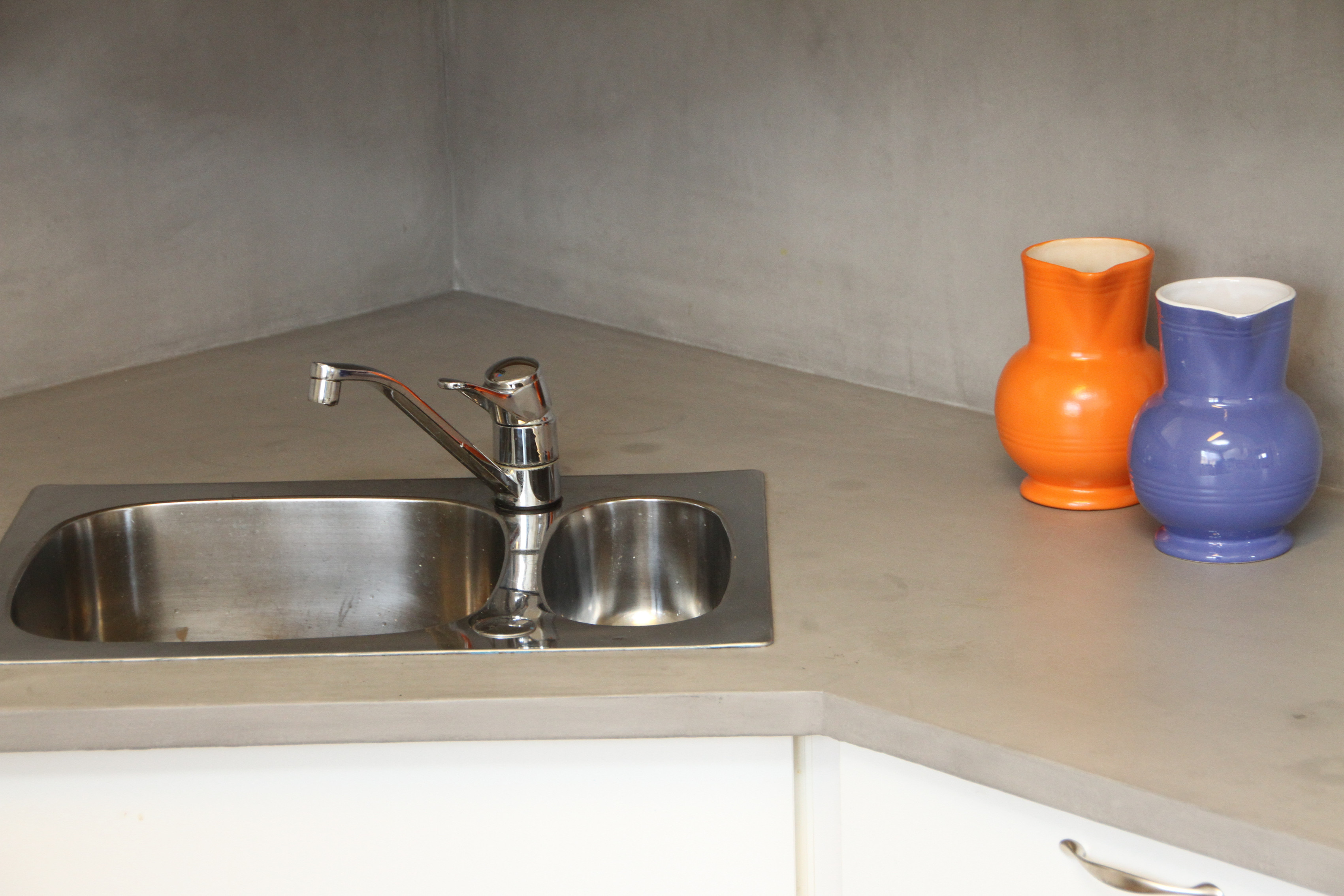 Benkeplaten på dette kjøkkenet var en gang en laminert sponplate. Den fikk etter hvert fuktskader og begynte å svelle. Vi freste bort skadene og valgte å gi den nytt liv med betongpulver, før vi forseglet med PU-lakk. Resultatet ble røft og stilrent. 