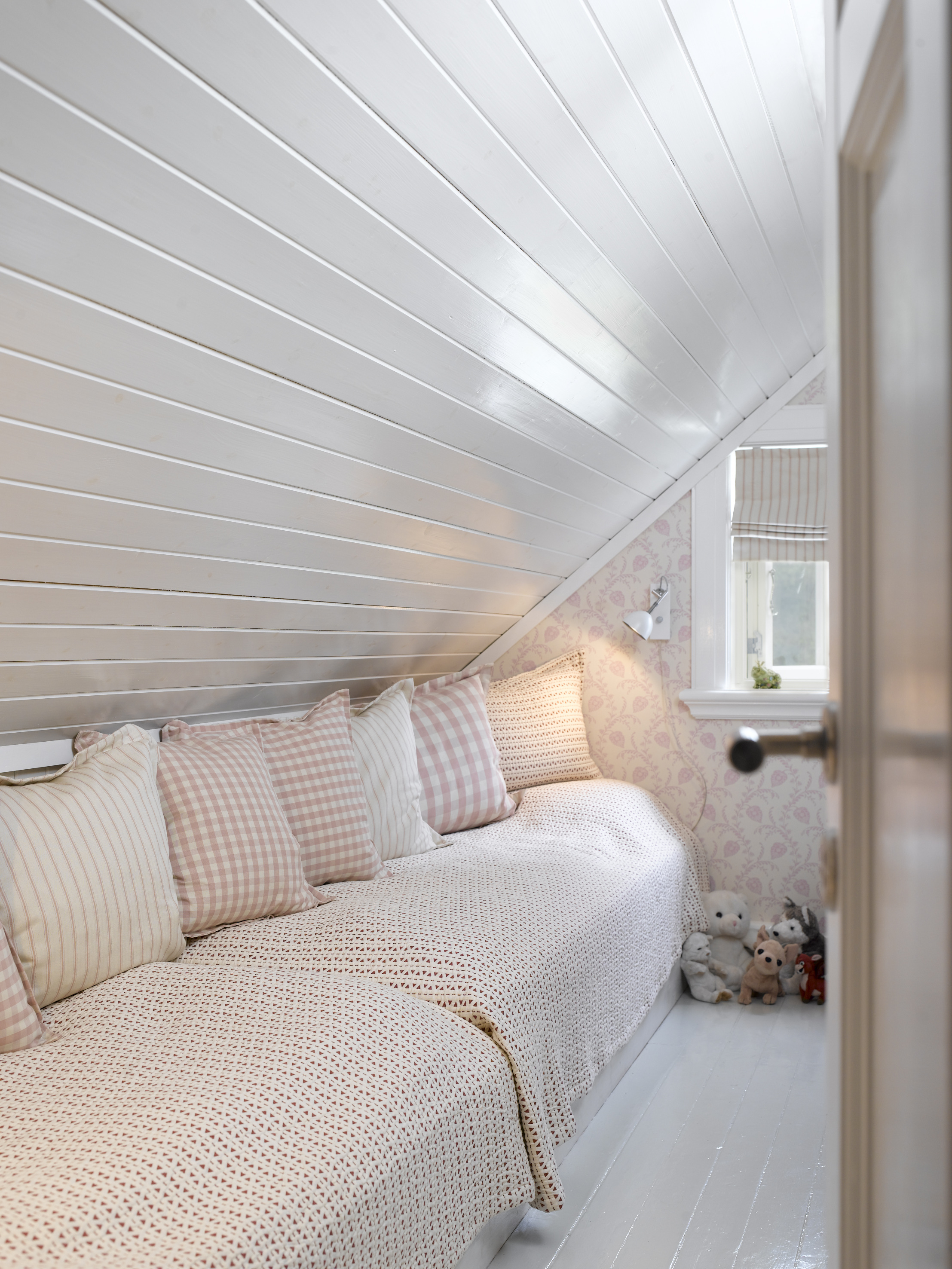 Jenterommet er et lite rom, som med blankt, hvitmalt tak og gulv virker større. Duse rosafarger på tapet- og tekstilmønstre understreker den feminine og delikate stilen. 