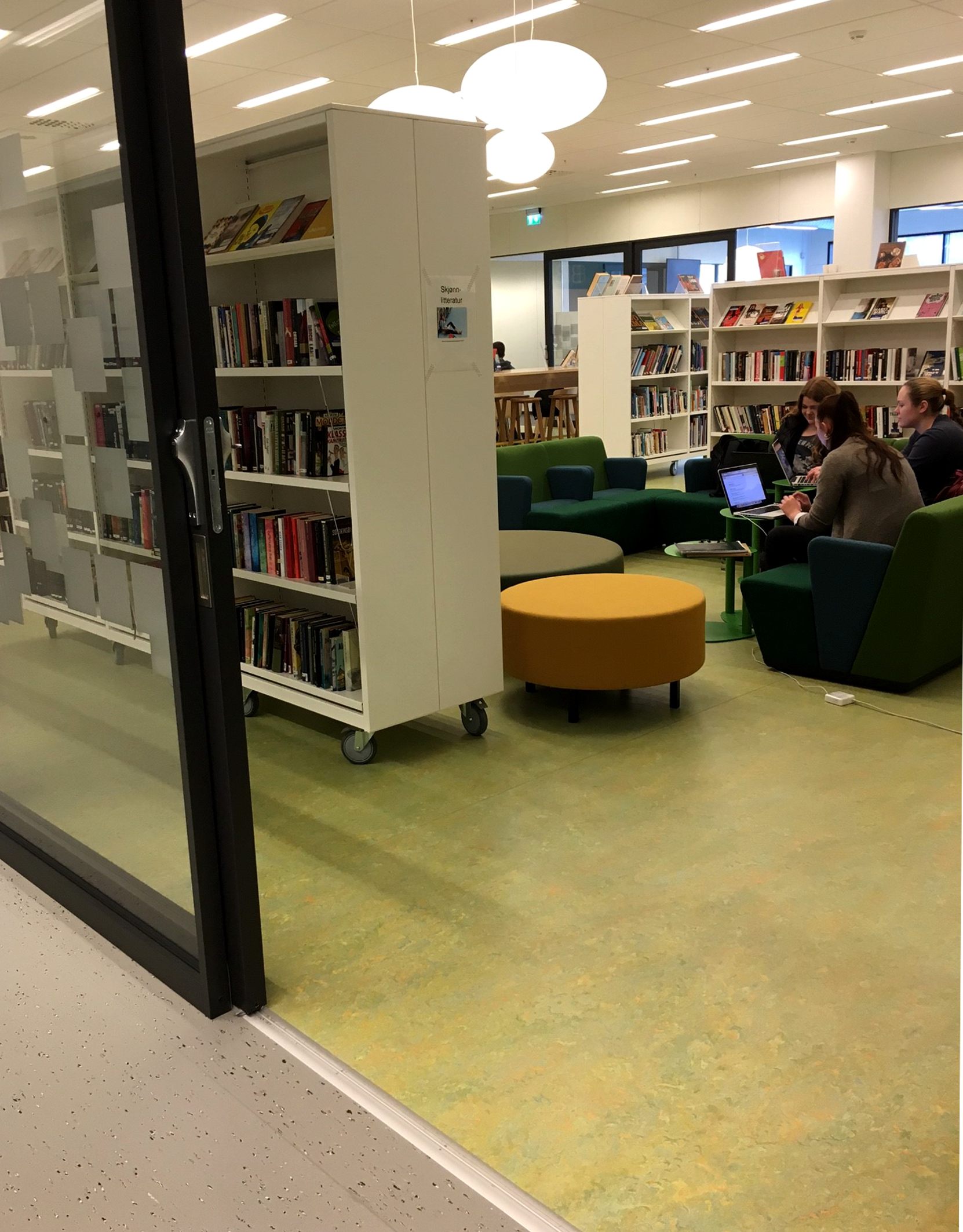 DEMPET INSPIRASJON: I bibliotekets bokavdeling er det rolig aktivitet, og her er det lagt et surgrønt gulv, i designen Vivace. Korridoren utenfor har gråmelert belegg, som i andre generelle arealer. 