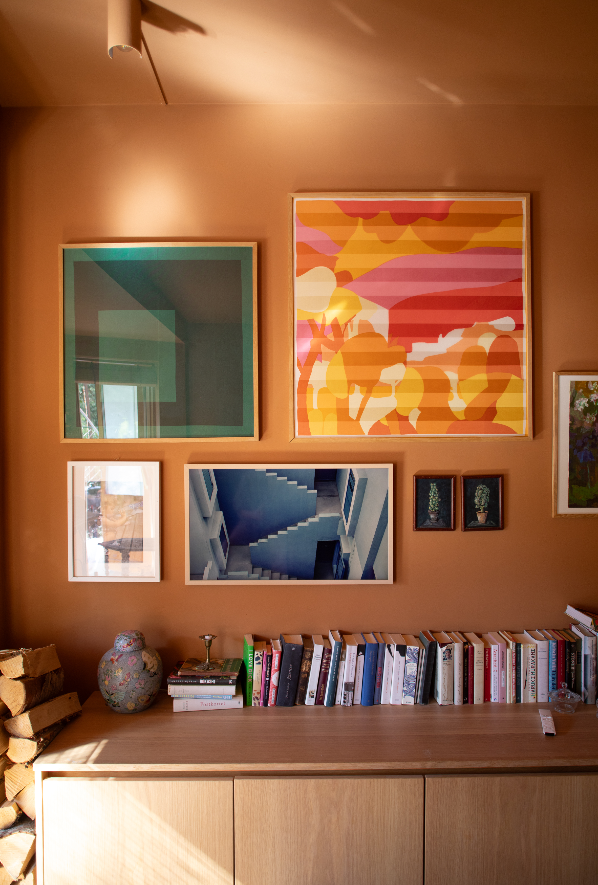 oransje vegg med flere malerier og en benk foran