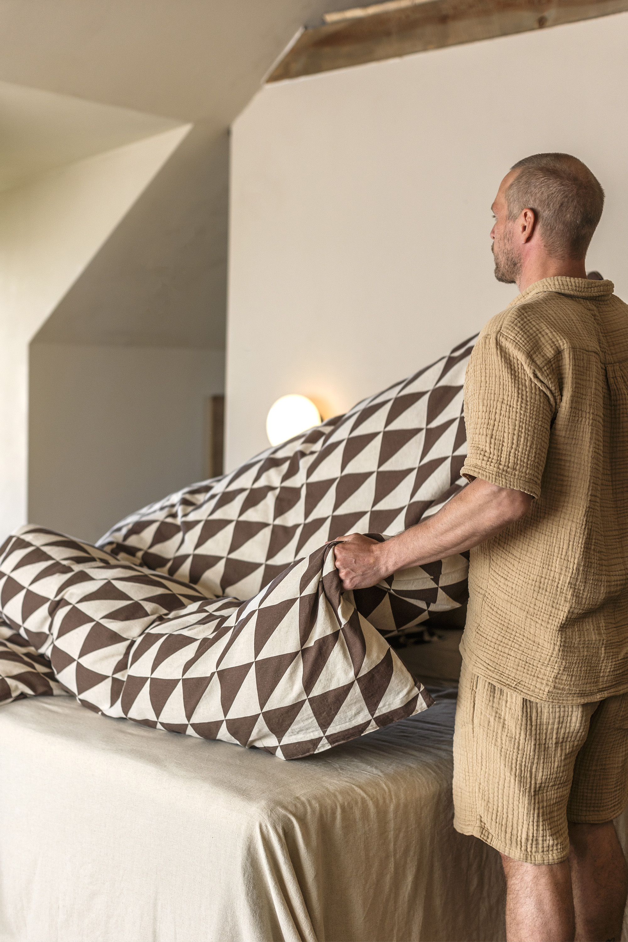 mann står ved sengen og løfter dynen