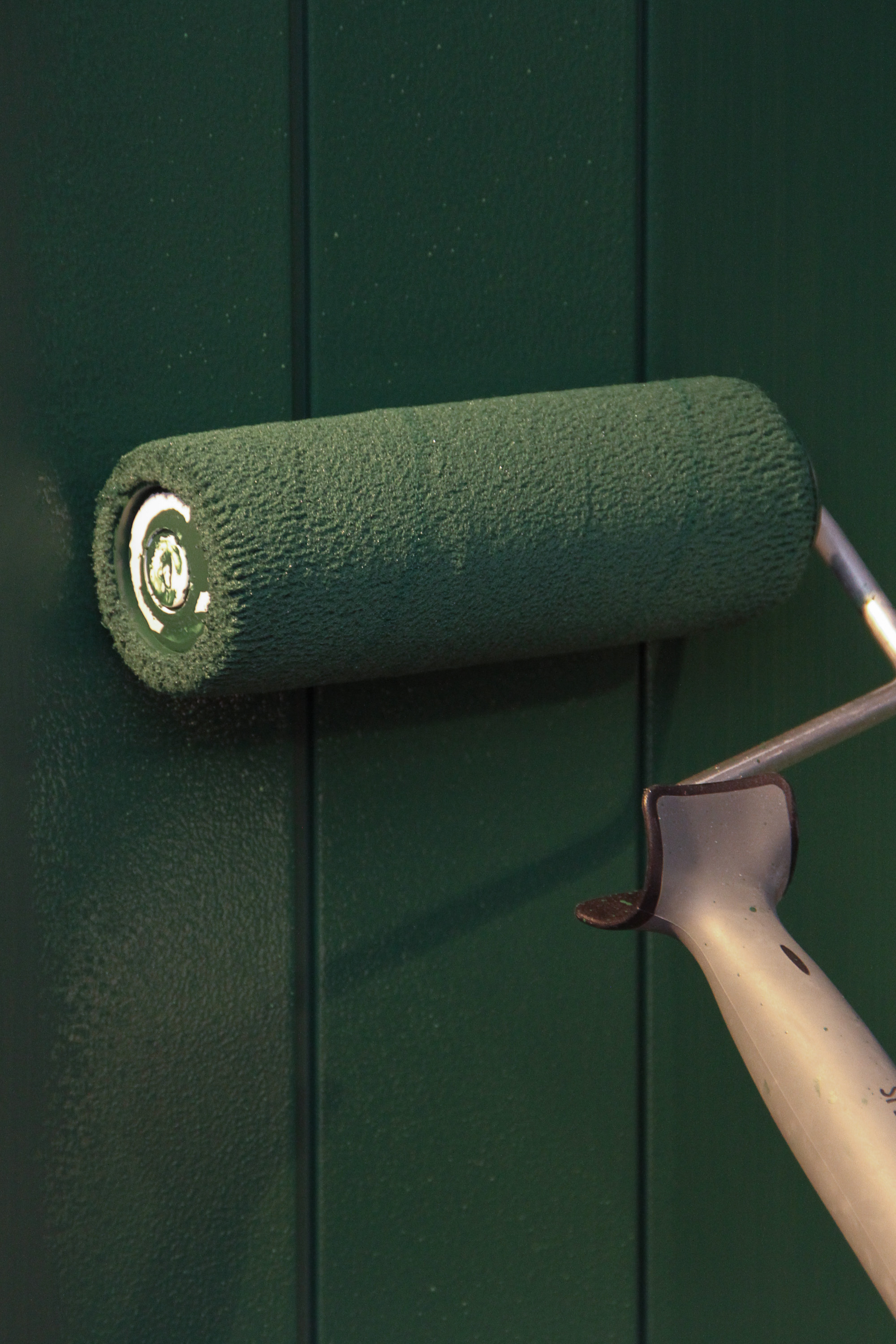 Malerull brukes og påfører en grønnfarge til en panelvegg.