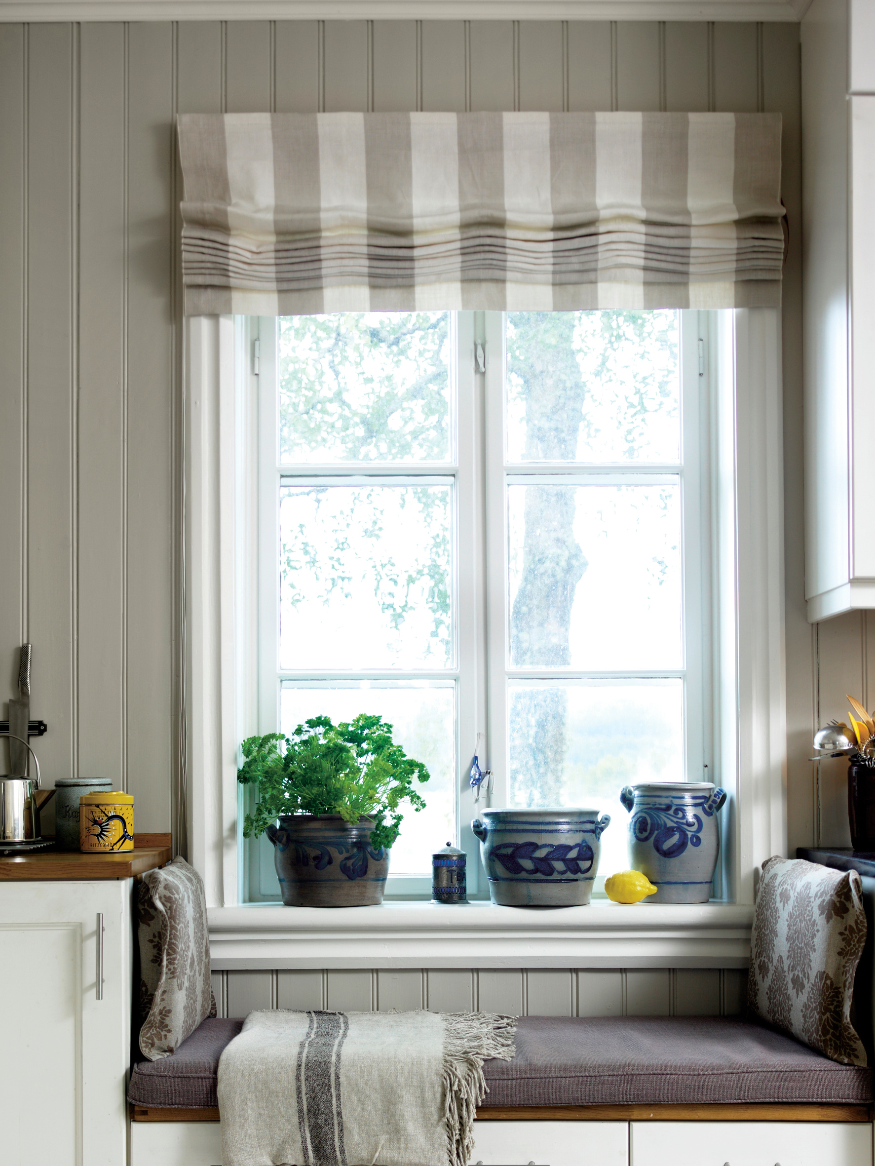 PLASS FOR TO: Benken er en del av kjøkkeninnredningen, hyggelig plassert foran vinduet. Arbeidsbenker i normal høyde på begge sider. Puter og pledd myker opp blant de rette linjene. 