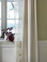Tette gardiner henger inn mot veggen, mens nærmest vinduet er det et transparent tekstil, som slipper gjennom lyset. 