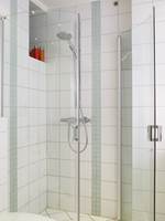 En dusj kan ta stor plass i et lite bad. Men lure løsninger som denne, med glassdører som kan slås inn, hjelper. Dørene er buet, og gjør det lettere å passere om det er to som bruker badet på samme tid. Legg merke til stripene som er laget av to bredder mosaikk.