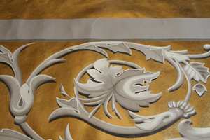 Detalj av linlerret forgylt med slagmetall. Dekoren er malt med linoljemaling som en illusjon av stukkornamenter. Lerretene ble montert på finer og dekker gallerifrontene i gamle Drammen teater. 