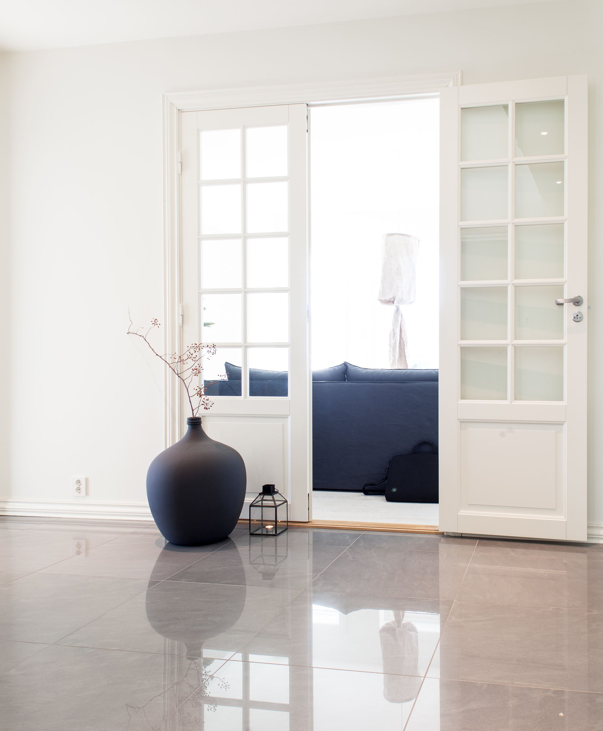 Gangen fører inn til en stue med mørke farger, som krukken i gangen tar opp. Dørene slipper gjennom godt med lys, som reflekteres i gulvet. 