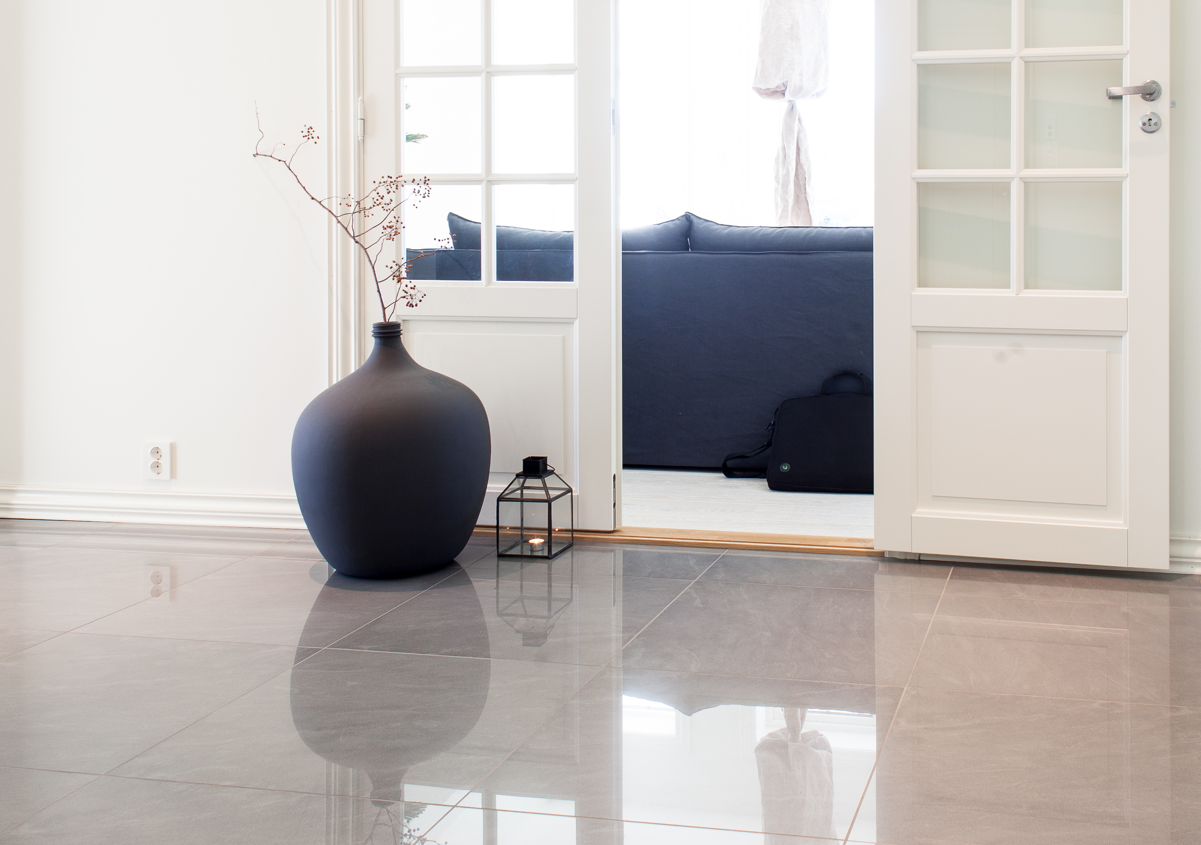 ROM P&Aring; ROM Fra hallen ser man inn i en av stuene, med samme veggfarge og m&oslash;rke m&oslash;bler. Den sorte krukken refererer til m&oslash;blene, og blanke gulvfliser reflekterer lyset.