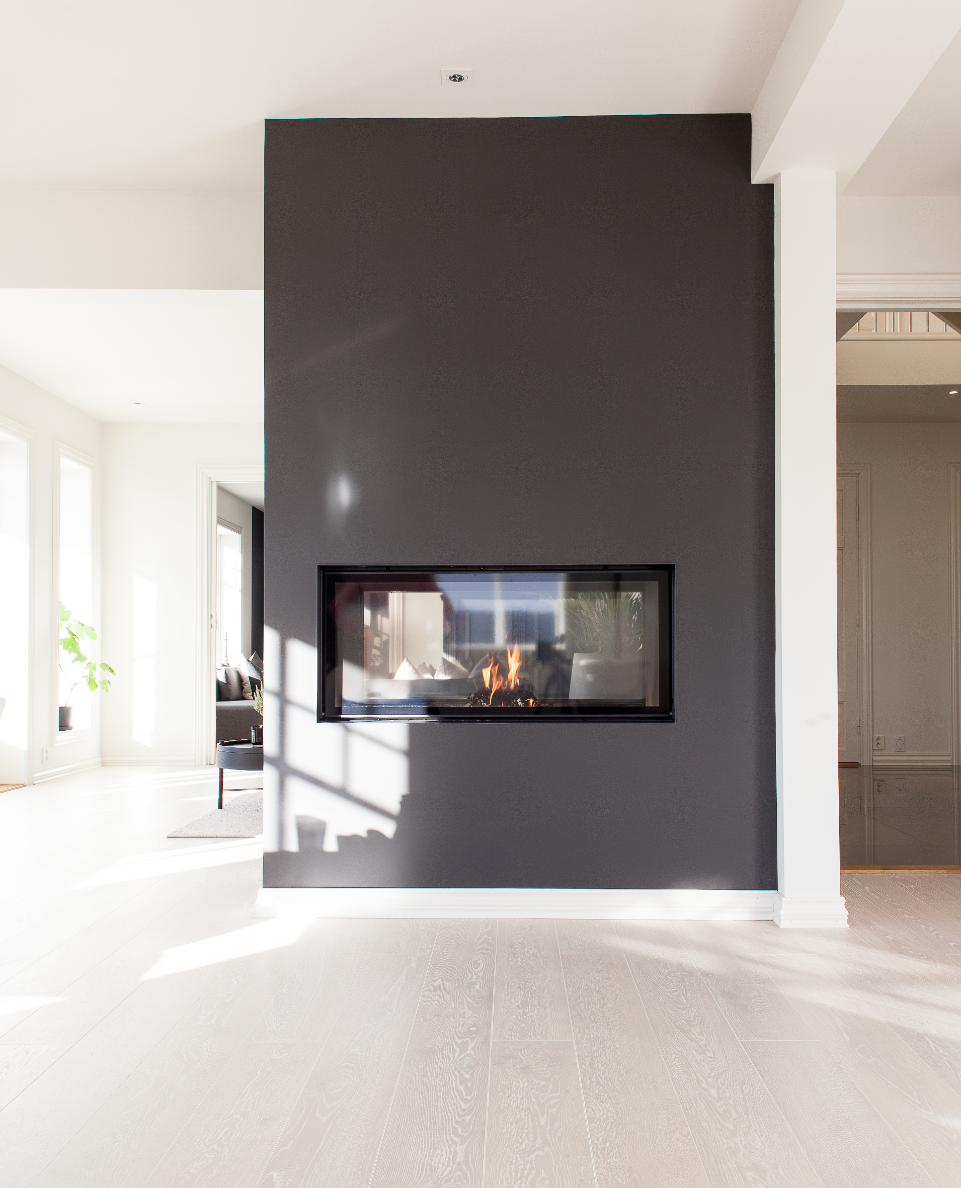 Peisveggen er fremhevet i en mørk gråfarge, og blir på den måten en større del av interiøret. Den fungerer også som en staselig romdeler. Ilden synes fra begge kanter. 