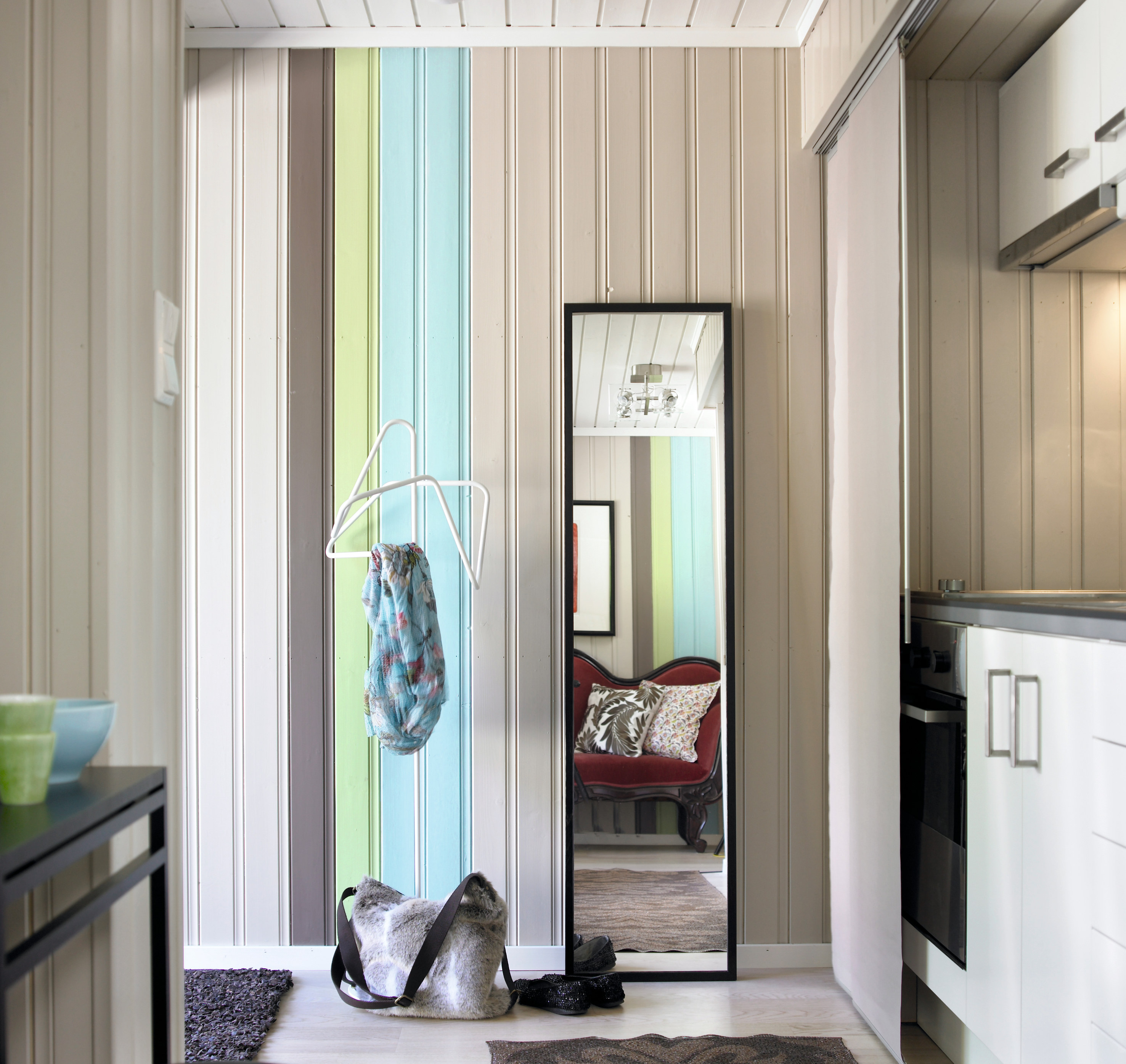 Entréens fargefeltet har tre farger; S 6005-Y50R (brun), S 2030-G50Y (grønn) og S 1020-B10G (turkis). Det er kort vei til stuen (i speilet), hvor panelet (S 2005-Y30R) har fått samme dekor. Stripene strekker veggene og øker følelsen av takhøyden.   