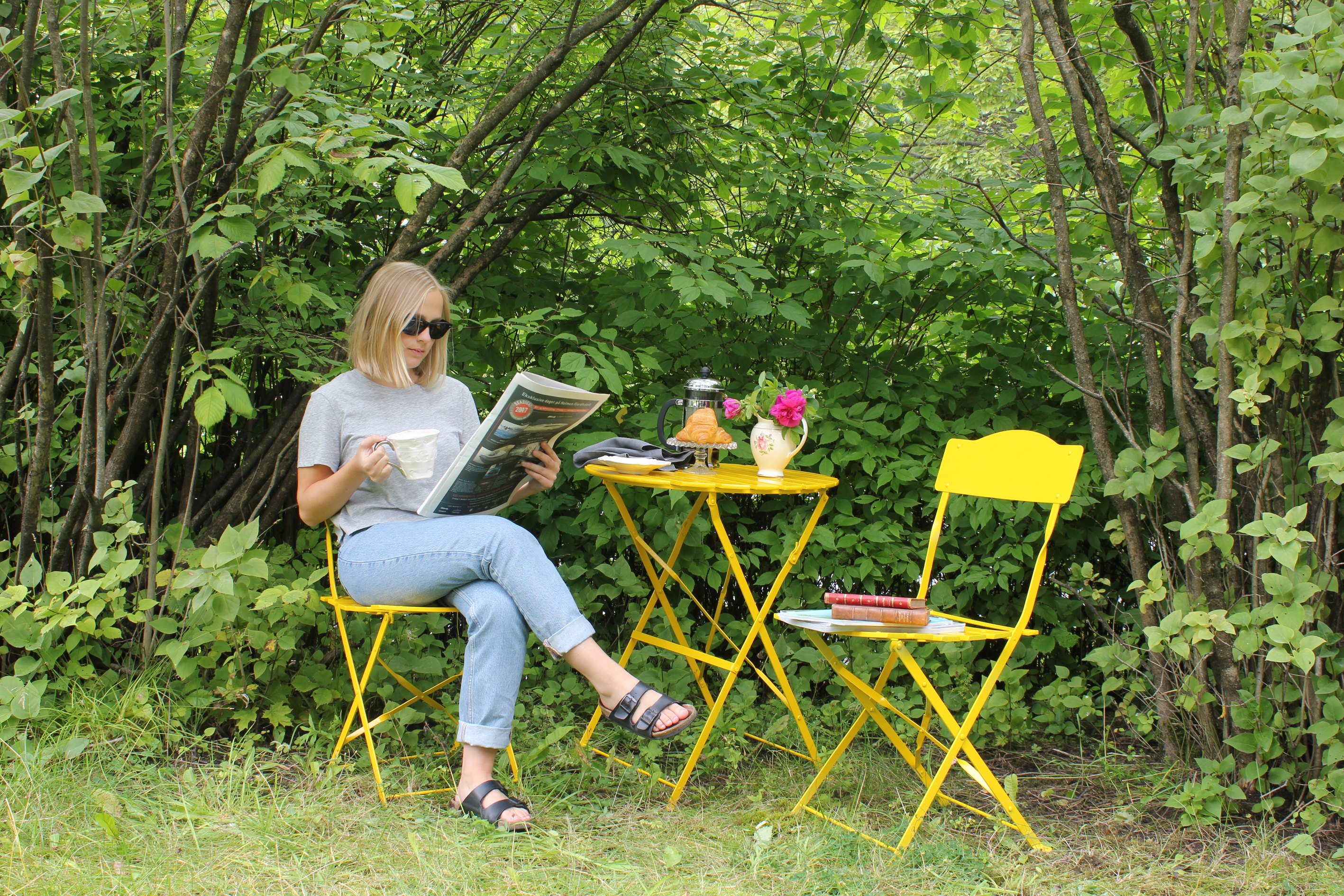 Ung kvinne leser i gule utemøbler 