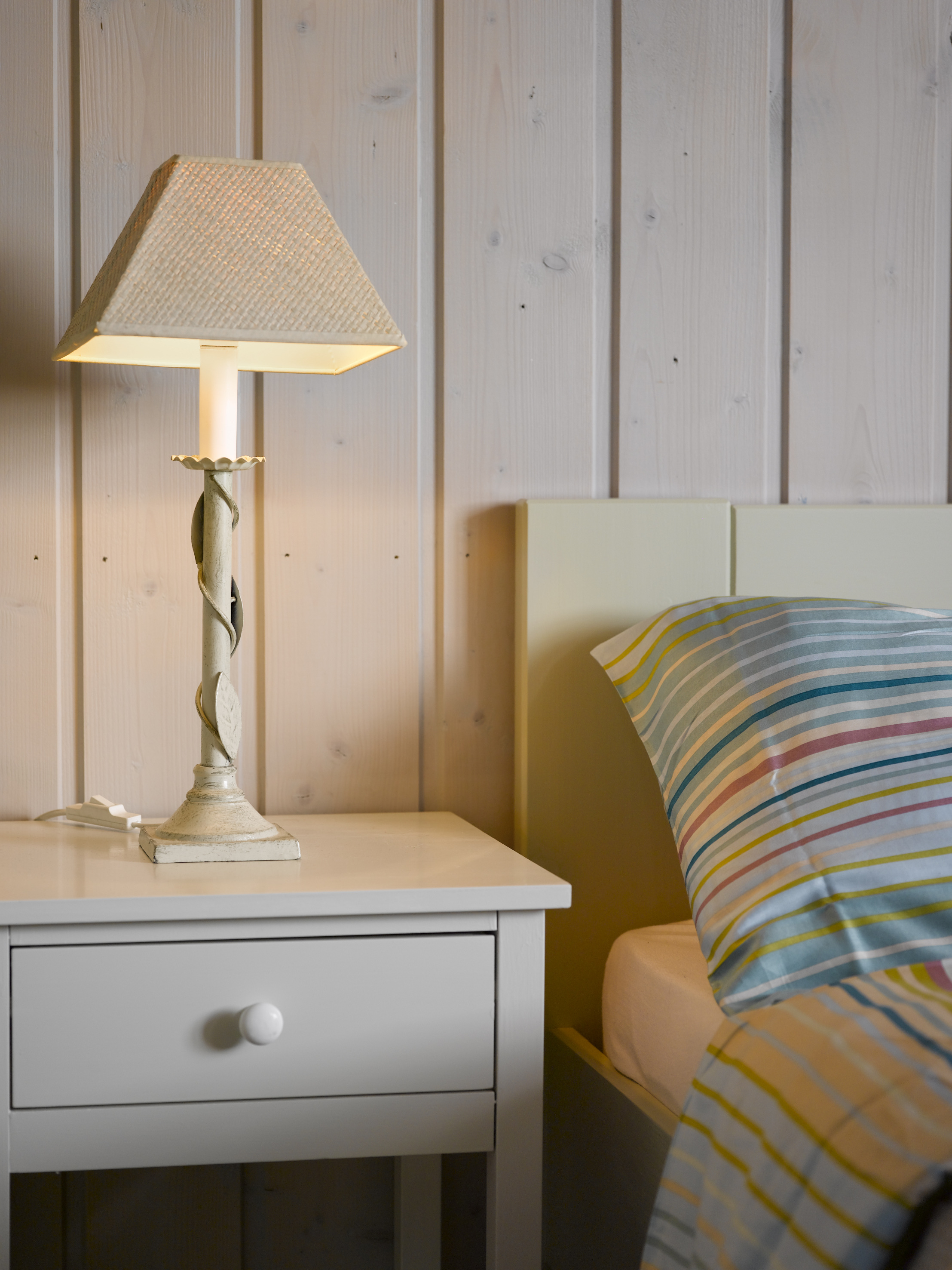 En dempet gråfarge på veggen, som slipper gjennom trestrukturen, i fint samspill med gråmalt nattbord og lysegrønn seng. 