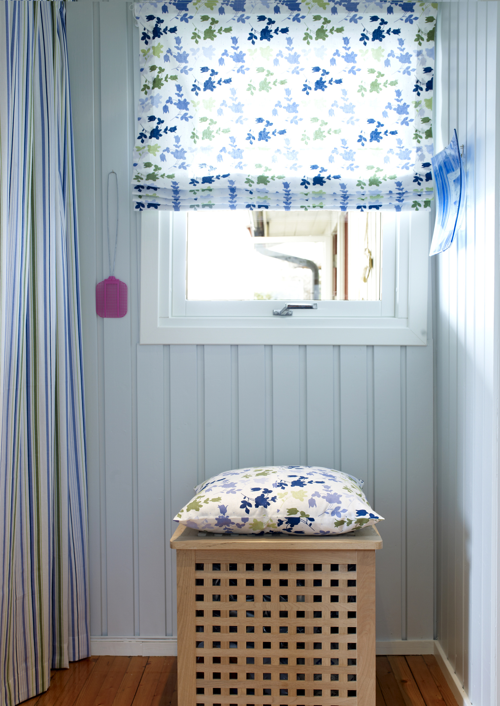 Alltid beredt – fluesmekkeren henger klar! Mer forheng og gardin, i samme tekstiler som ved benken. Skittentøysdunken har fått en pute, og fungerer også som sitteplass. 