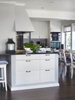 Kjøkkeninnredningen har hvitmalte panelte fronter og grove håndtak som gir et landlig preg. 