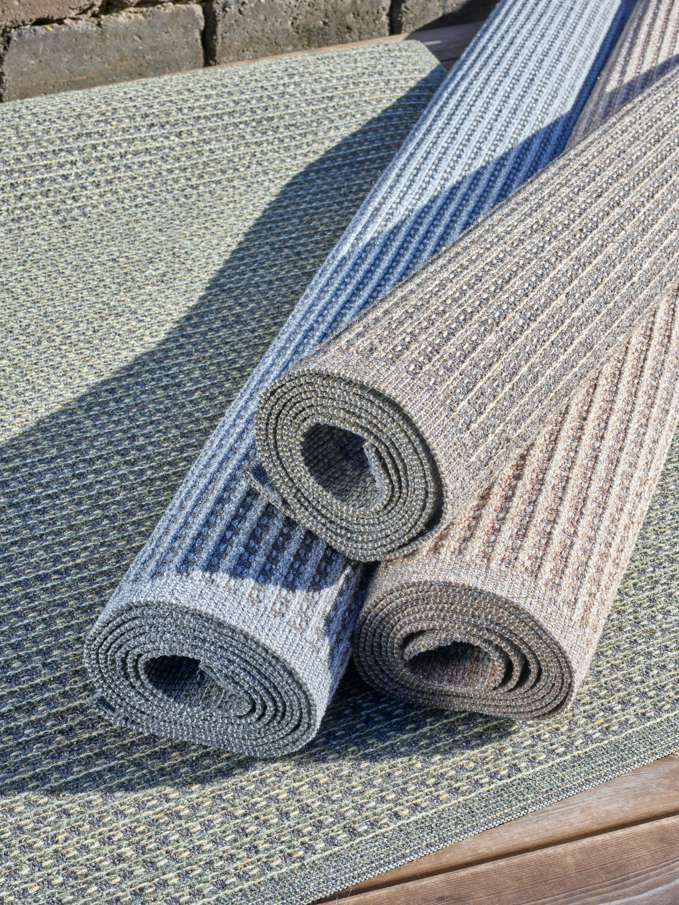 tre ruller med utetepper ligger på et fjerde teppe på en treterrasse