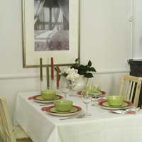 Spisebordet er plassert slik at alle fire plassene har utsikt over rommet og. Tilsvarende bord og stoler står på kjøkkenet slik at man kan lage et langbord i stuen når det skal dekkes til fest. Dekketøy i rødt og grønt er varme og friske fargeinnslag i de lyse omgivelsene. Den hvite duken er impregnert med et flekkavstøtende middel. 