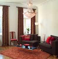Øisteins rom: Den innerste stuen fikk et varmere uttrykk ved hjelp av tykke, klassiske gardiner, fyldige, mørkebrune modulstoler og et rufsete oransje teppe. Puter i varmrosa og lilla setter et feminint preg på leilighetens nye 
