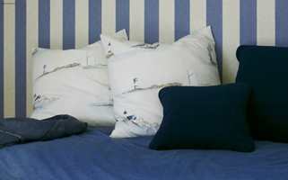 Detalj av sengen med jeans-sengeteppet og puter i samme tekstil som gardinen.