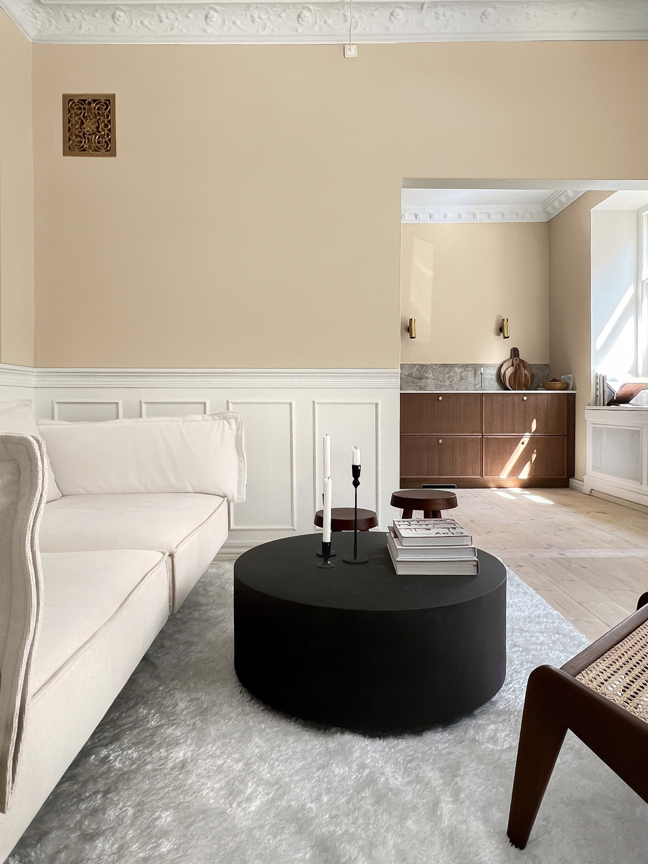 sofa med sort puff i et rom med døråpning og beige vegger med hvit brystning.