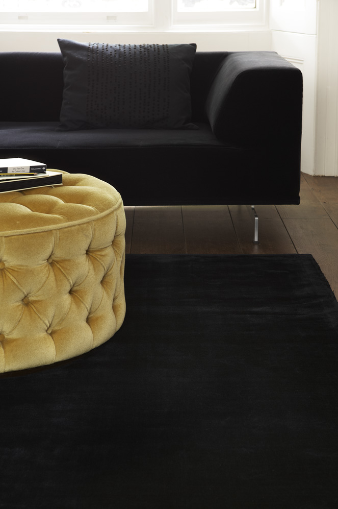 TØFFE KONTRASTER: Lekkert med sort teppe mot ditto sofa og gul puff. Teppet fra Jacaranda og INTAG gjør godt for føttene.  
