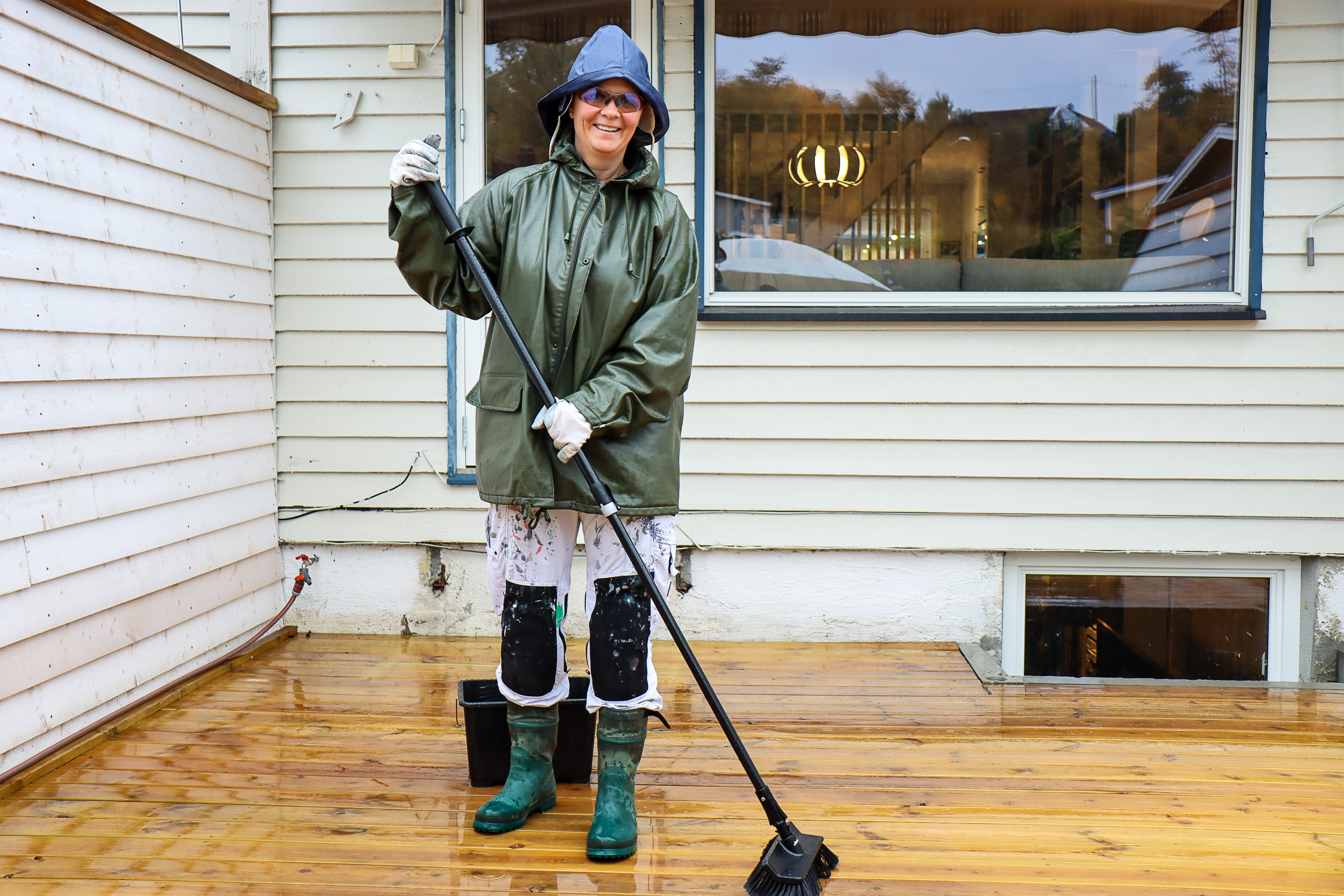 mann i regntøy skrubber treterrasse mens det regner