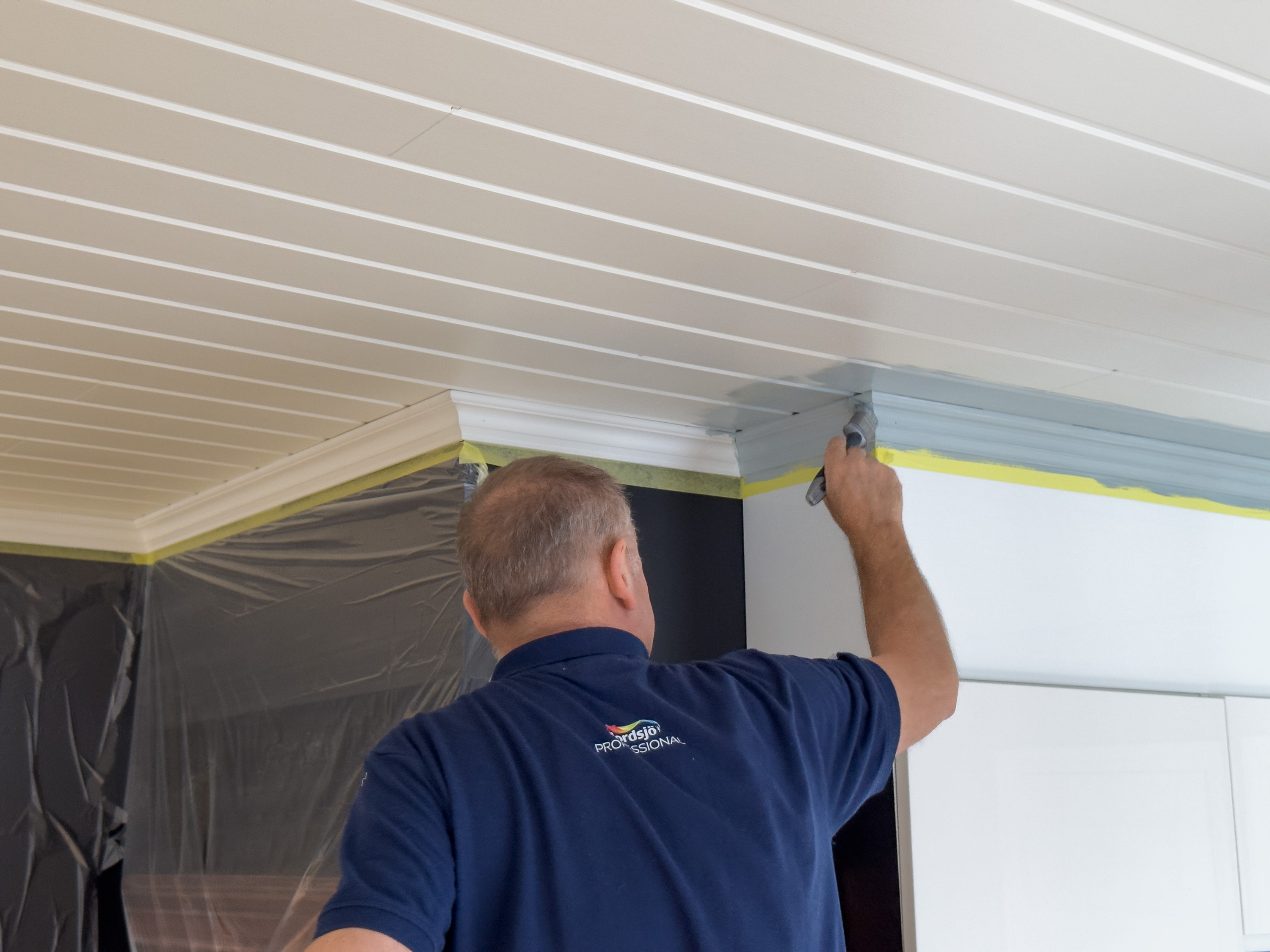 Per Myhre maler taklistene og kantene av panelet.