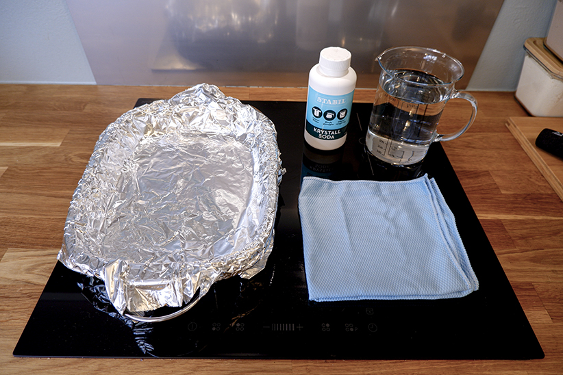 Krystallsoda, vann, aluminiumsfolie, noe å legge sølvtøyet oppi, mikrofiberklut.