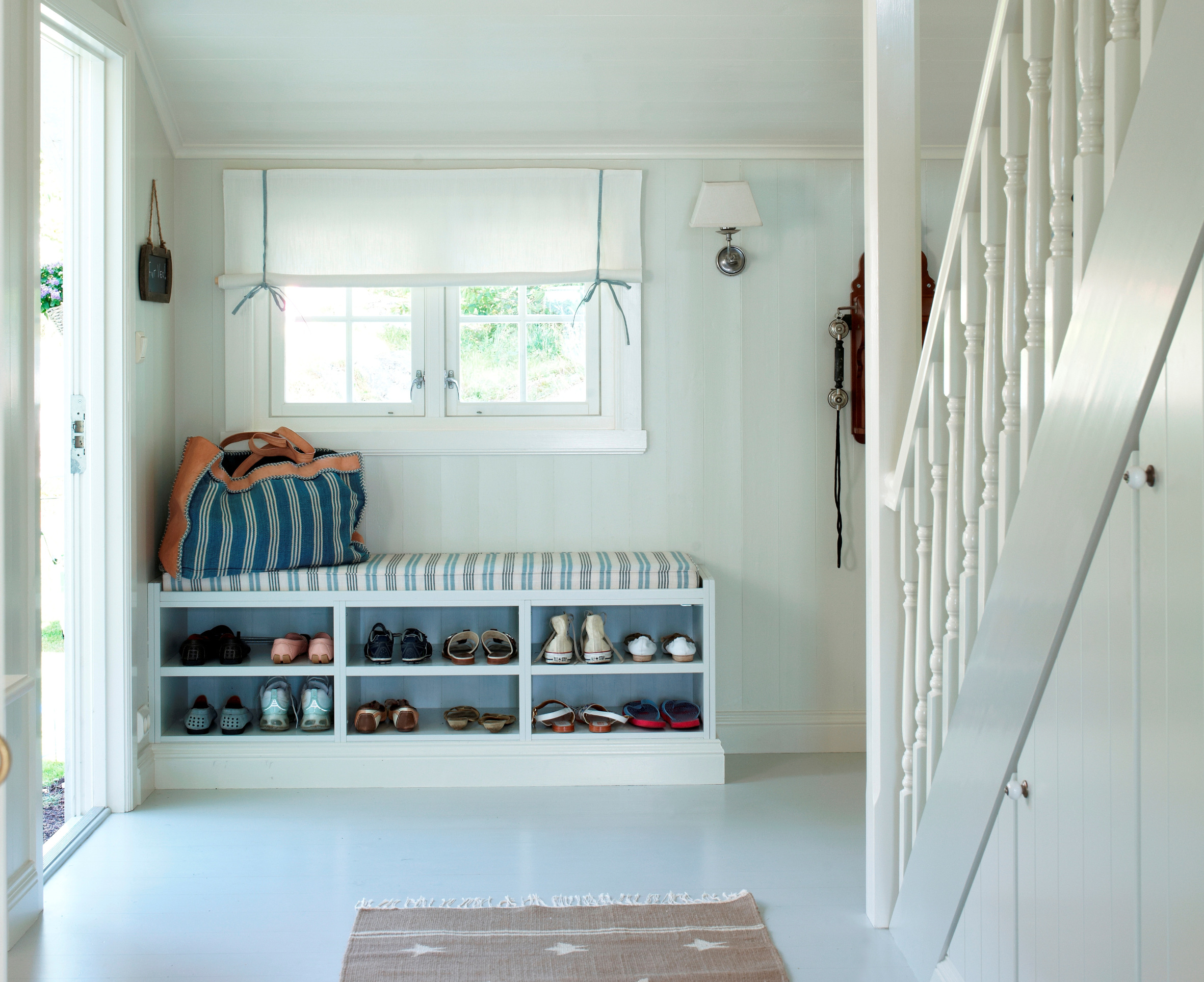 En praktisk skohylle med sittebenk  er bygget på stedet, og holder orden i familiens skotøy. Liftgardinens tynne tekstil slipper lyset delvis igjennom.  