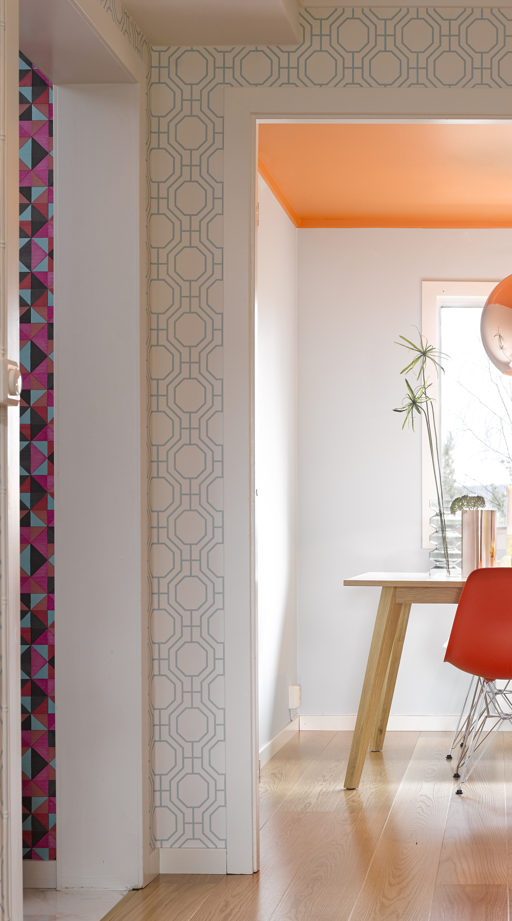 Fra stuen er det utsikt både til gangen og kjøkkenet. Oransjefargen i kjøkkentaket går igjen i tapetet i gangen, i en annen nyanse. Kjøkkenveggene har samme svale, blågrønne fargenyanse som i stue og gang – her råder full harmoni! 