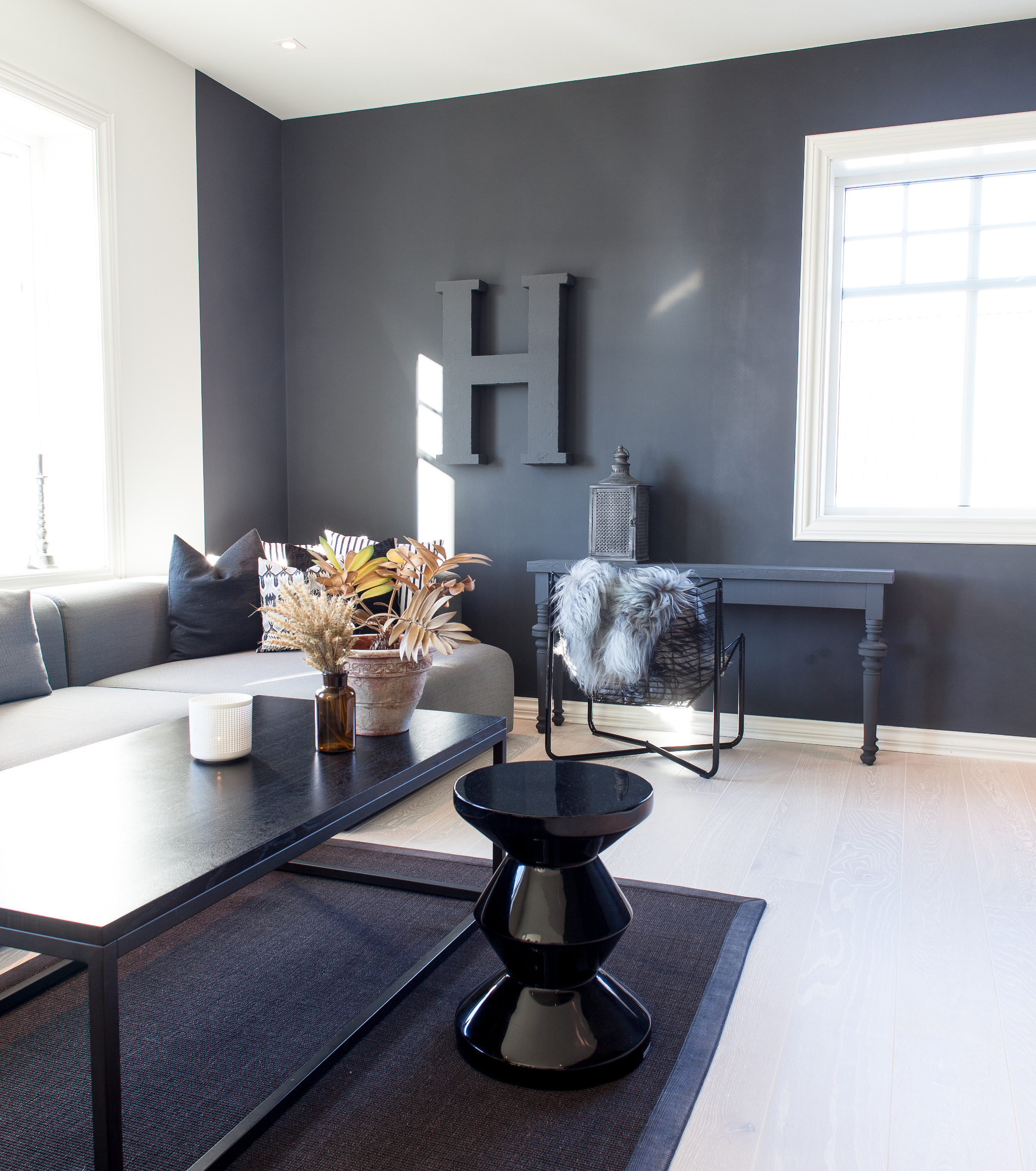 Spennende mørkt og aldeles ikke dystert. Mørke elementer på mørk bakgrunn skaper dybde. Taket og den lyse veggen er i varme hvitfarger, og gulvet har gjennomslag av trefargen – et forsiktig gyllent element. 