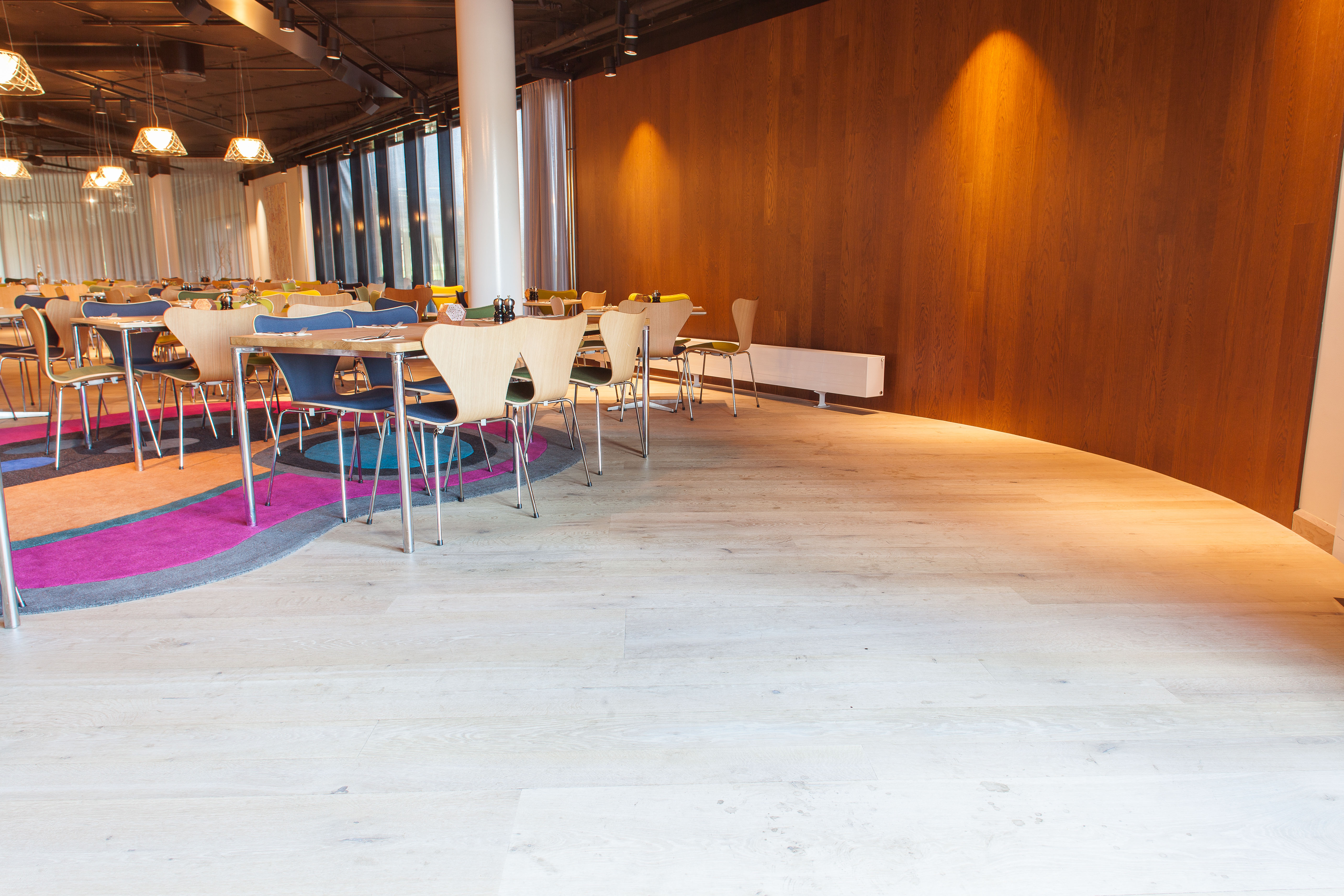 Frokostsalens lyse tregulv og mørke veggpaneler mykes opp med avrundede innredningsdetaljer og fargerike tepper.