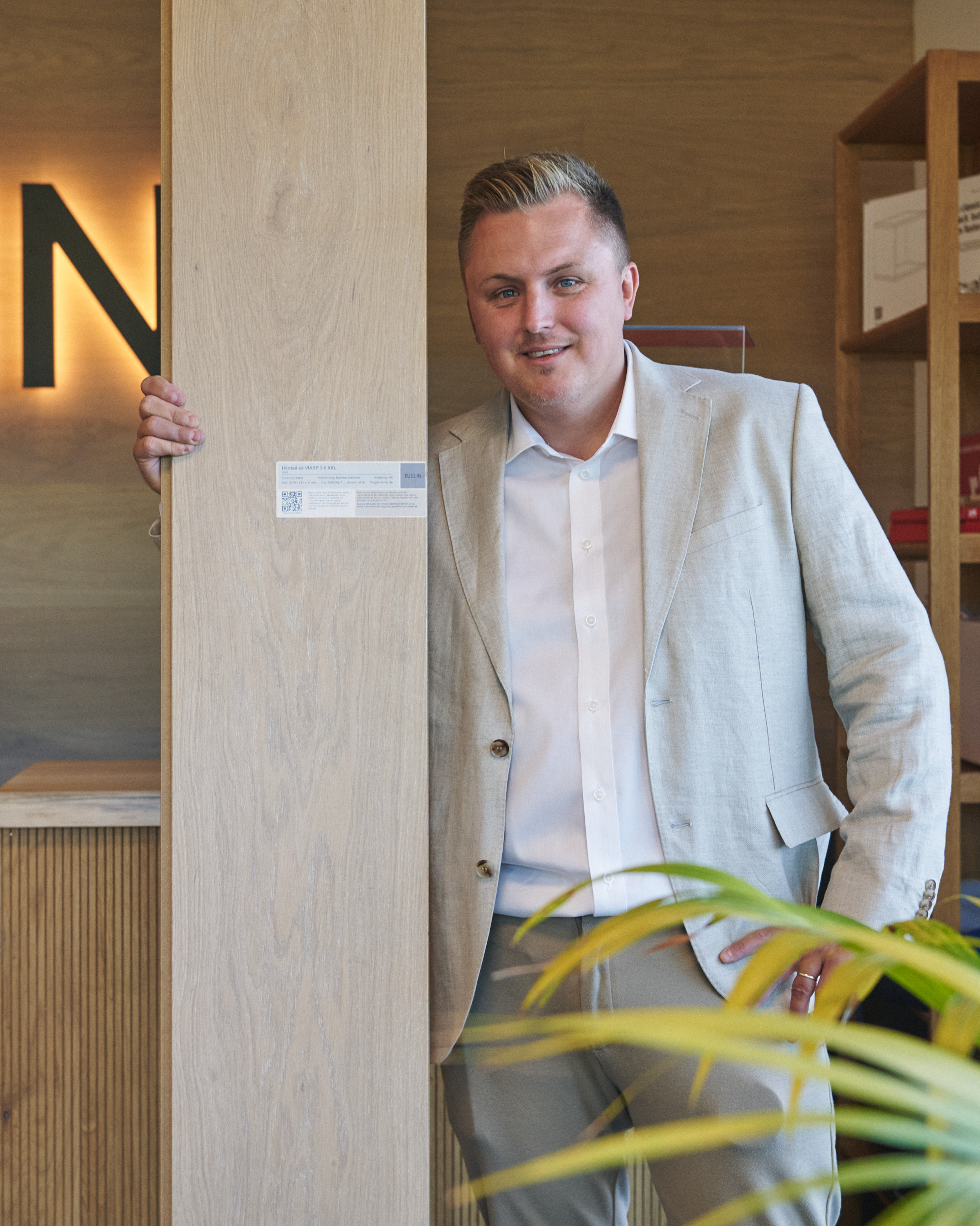 mann i beige dressjakke holder frem et bredt og langt parkettbord.