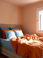PÅ TAK OG VEGGER - På soverommet har vi tatt opp den oransje tråden fra kjøkkenet, dog i en dempet, pudderoransje variant (S 1010-Y70R). Tak, vegger og listverk er malt i én og samme farge, noe som forsterker fargeeffekten. På bildet fremstår fargen mørkere enn i virkeligheten,
påvirket av lys og av sengetøy, sistnevnte reflekterer den kraftige
oransje fargen. Tekstilet på sengegavl og madrass oppsummerer fargene fra
de andre rommene i sitt geometriske mønster.