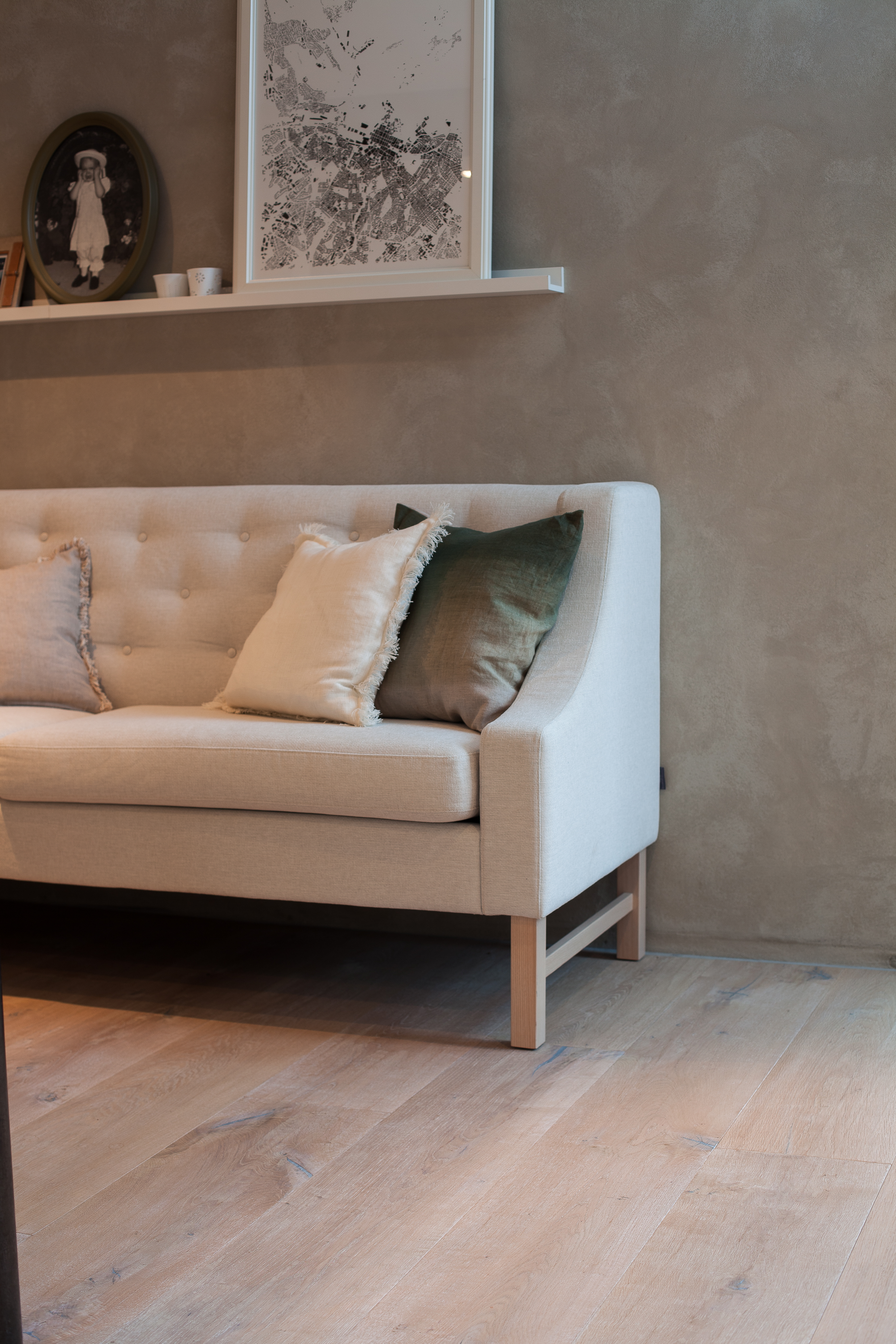 RØFF ELEGANSE: Sofaen står på kjøkkenet, vendt mot arbeidsplassen, og passer utmerket sammen med rustikke, ekstra brede gulvbord i hvitpigmentert eik og vegger i pusset mur. 