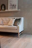 RØFF ELEGANSE: Sofaen står på kjøkkenet, vendt mot arbeidsplassen, og passer utmerket sammen med rustikke, ekstra brede gulvbord i hvitpigmentert eik og vegger i pusset mur. 