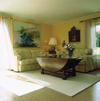 Sommerstue med lys sofa og lette gardiner og lyst teppe.
