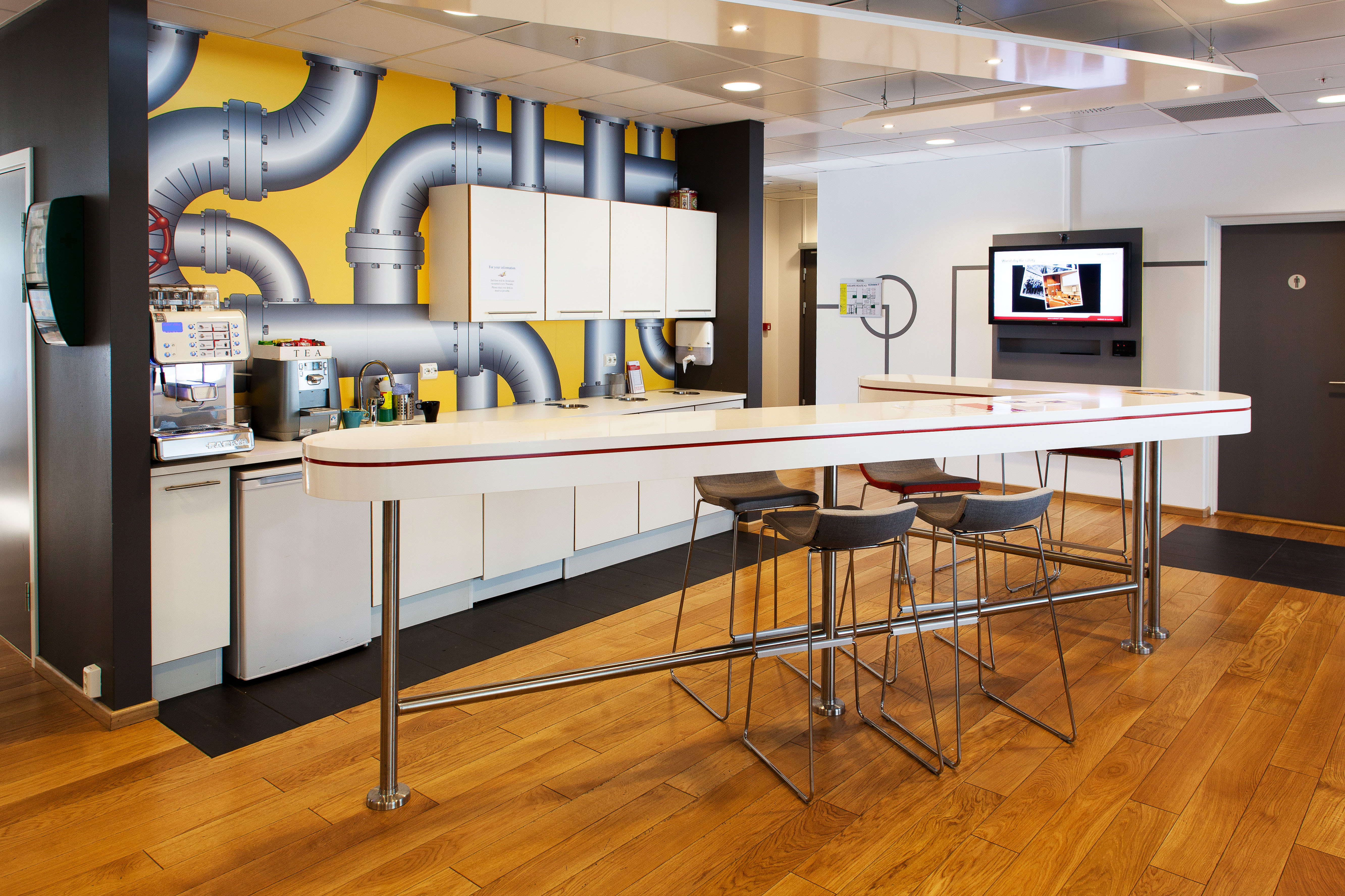 Tekjøkkenet er dekorert med bildetapet med høyst relevant motiv for å markere bedriftens virksomhetsområde. Legg merke til bordet som er formet som logoen - et syvtall.