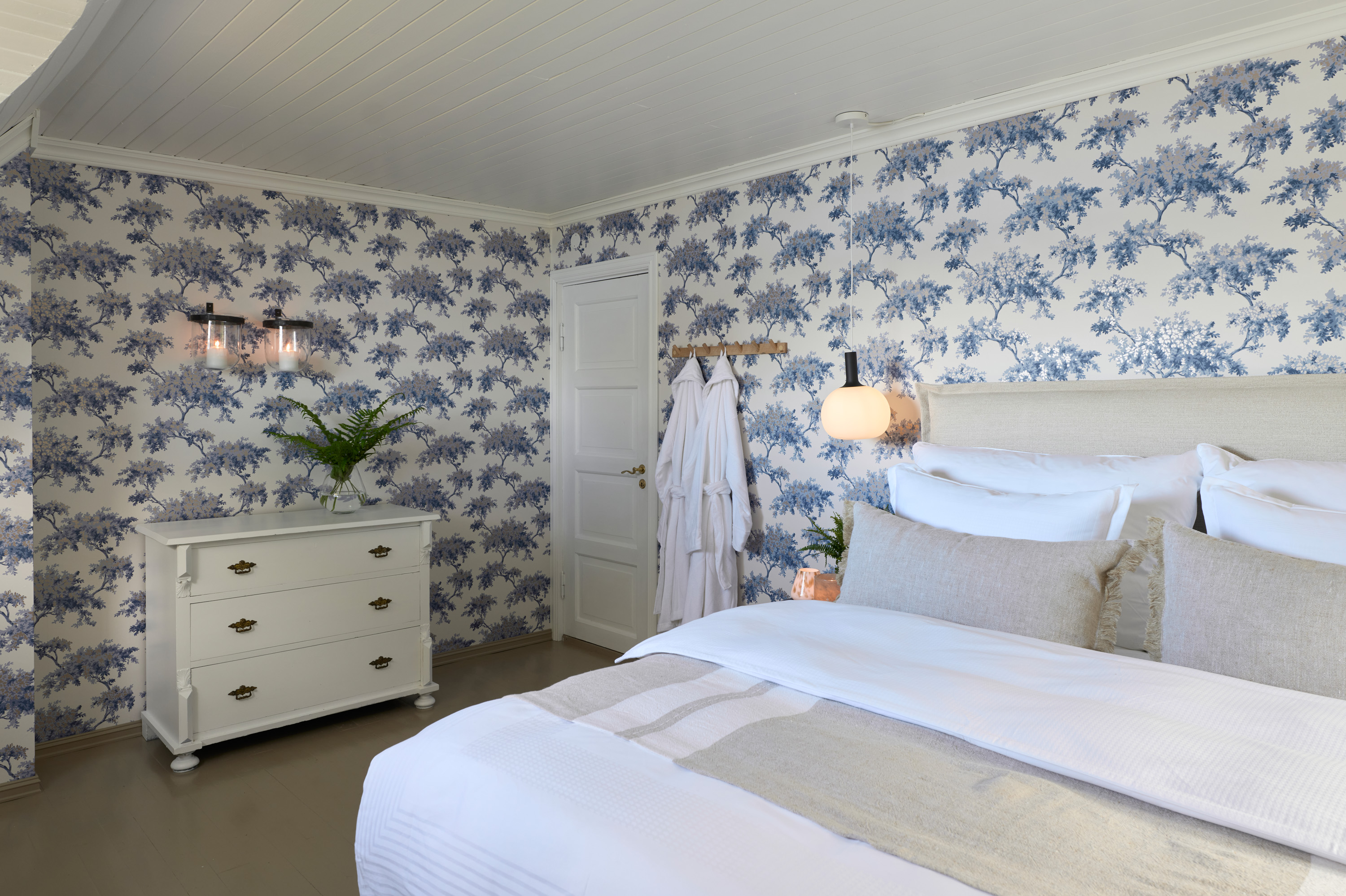 soverom med hvitt tak og hvite møbler. blått stormønstret tapet på veggene