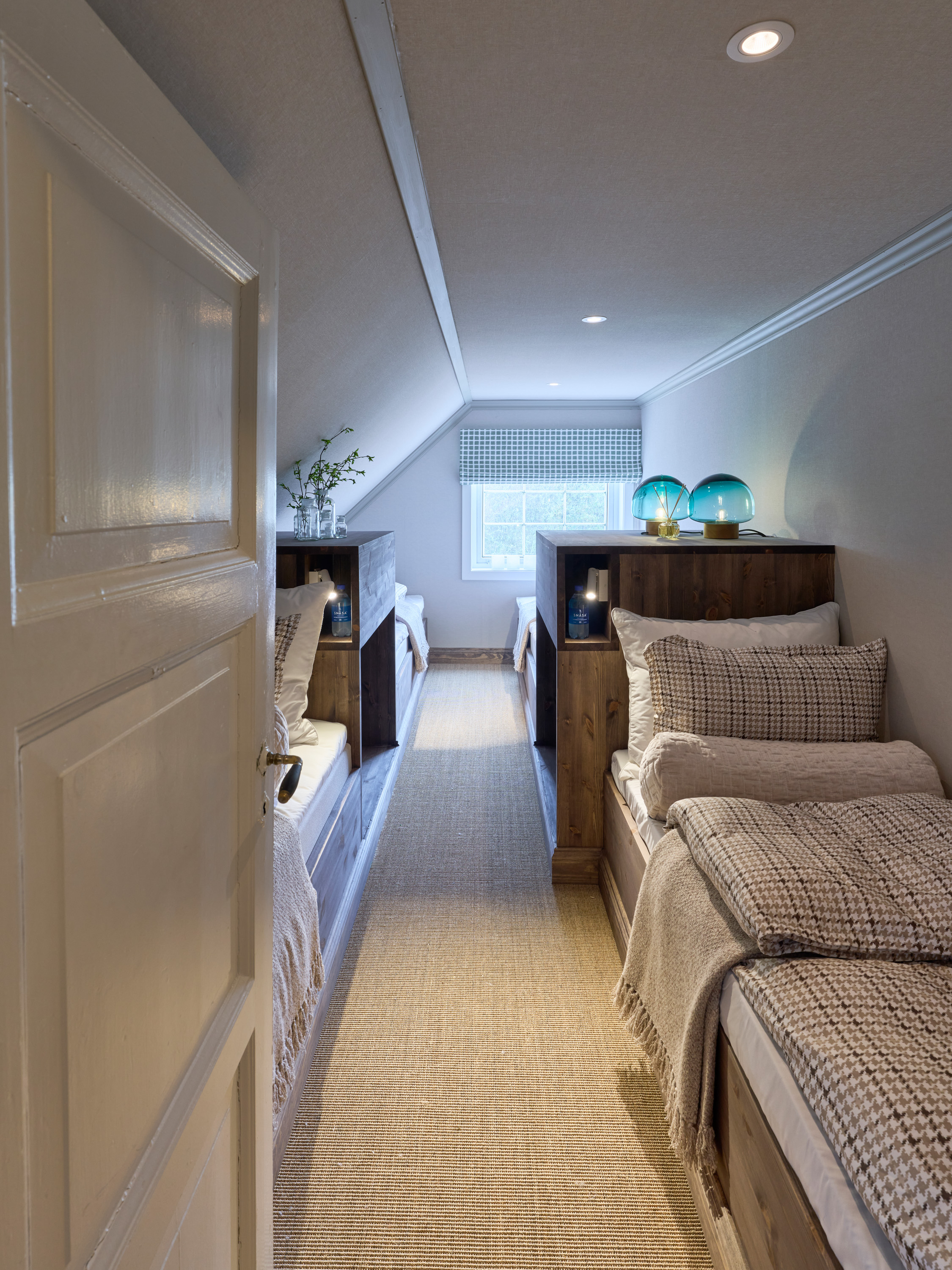smalt soverom med flere senger, tapet på vegger, tak og skråtak