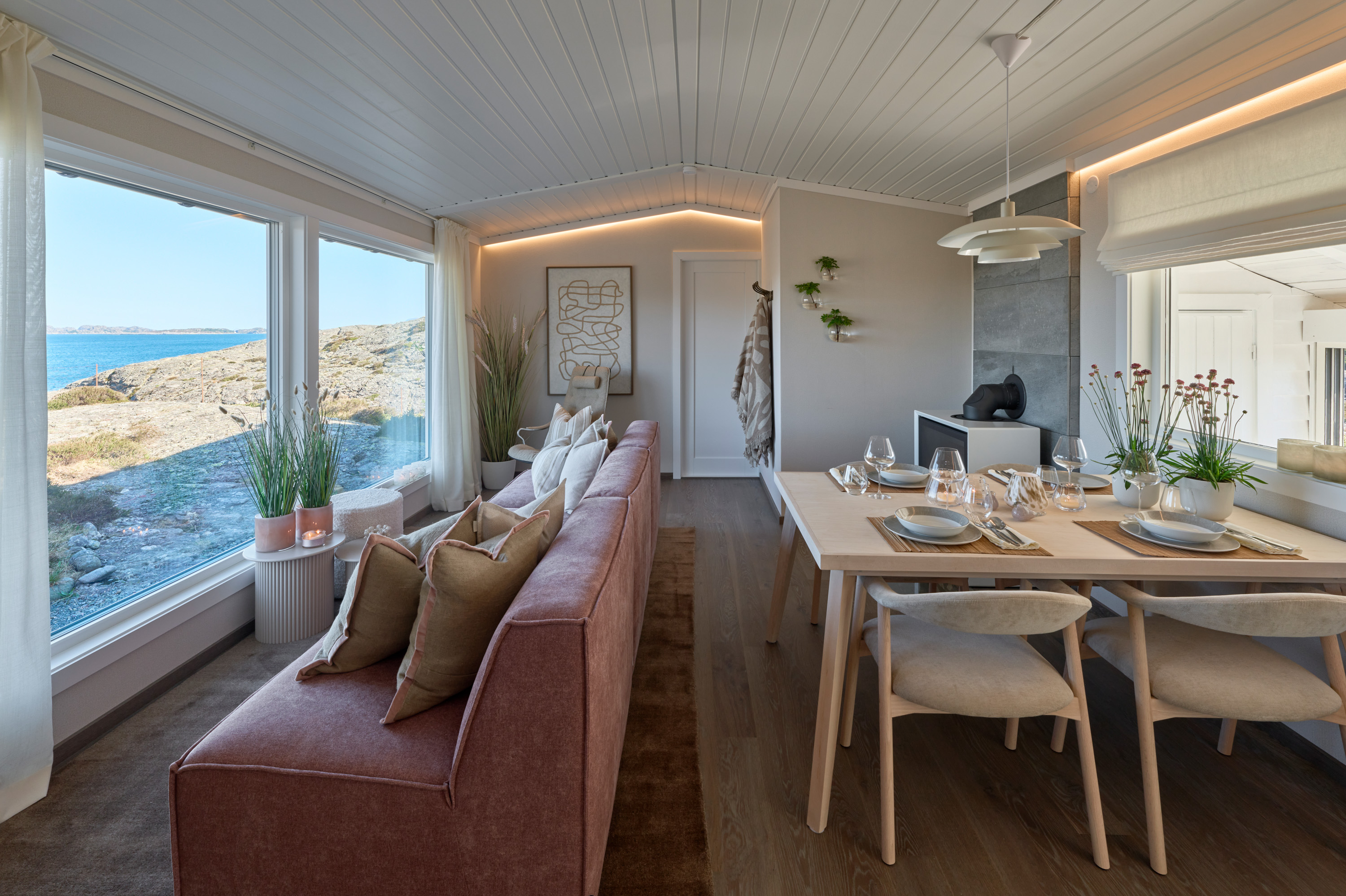 Stue i hytte med utsikt over svaberg gjennom store vinduer 