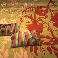 Igjen de kraftige mønstre på teppet i flotte, sammensatte jordfarger, matchende med puter i de like typiske blanke tekstiloverflater. Stripemønster er en gjenganger.