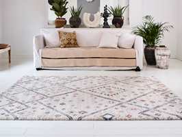 LUNT MED TEPPE: Det sandfargede teppet i sofaen, gulvteppet med lubben luv og rolig mønster, samt grønne planter gir den hvite stuen en hyggelig og innbydende atmosfære.