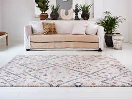 Det sandfargede teppet i sofaen, gulvteppet med lubben luv og rolig mønster, samt grønne planter gir den hvite stuen en hyggelig og innbydende atmosfære.